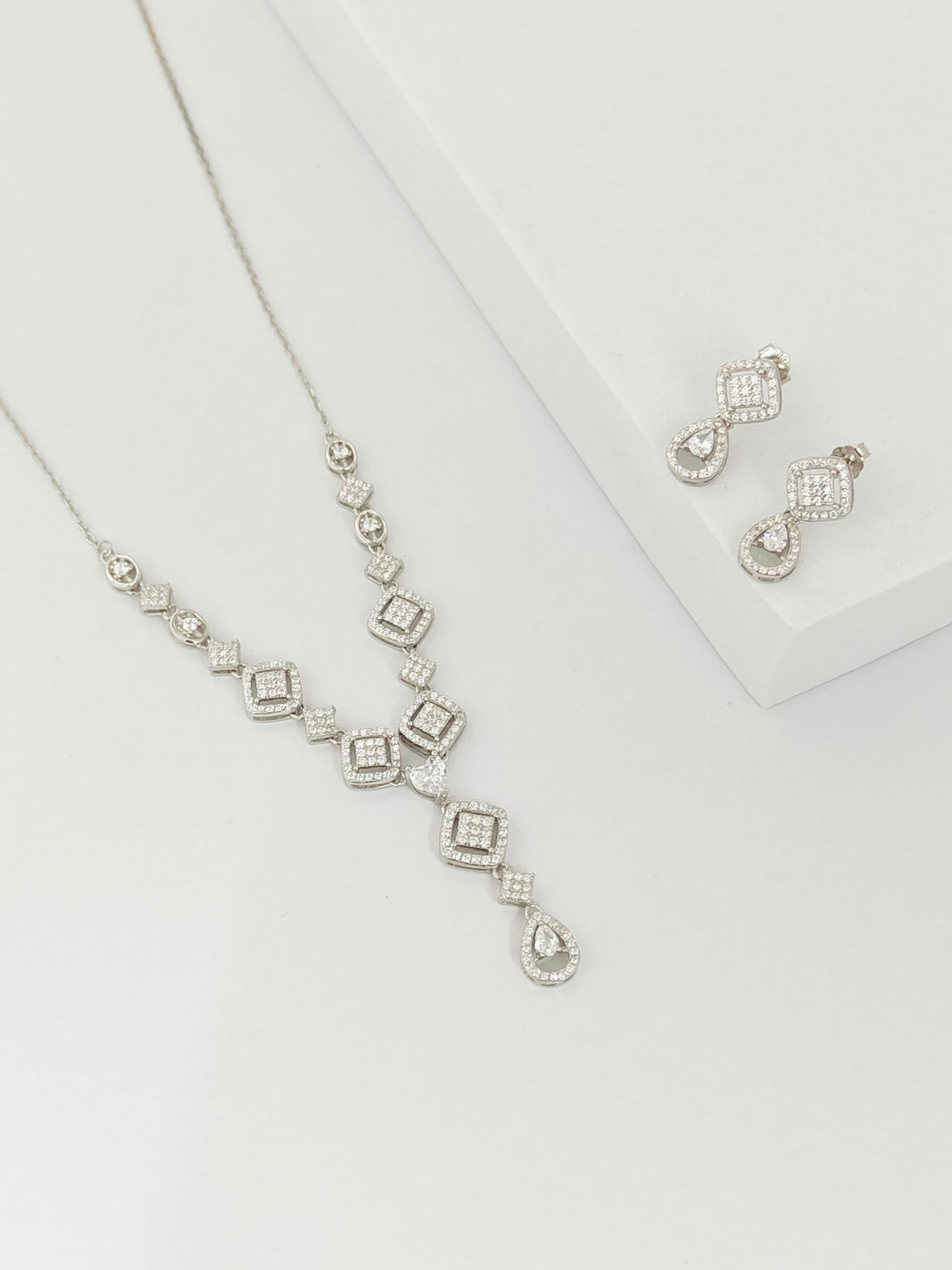Silver necklace and earrings on a light gray background