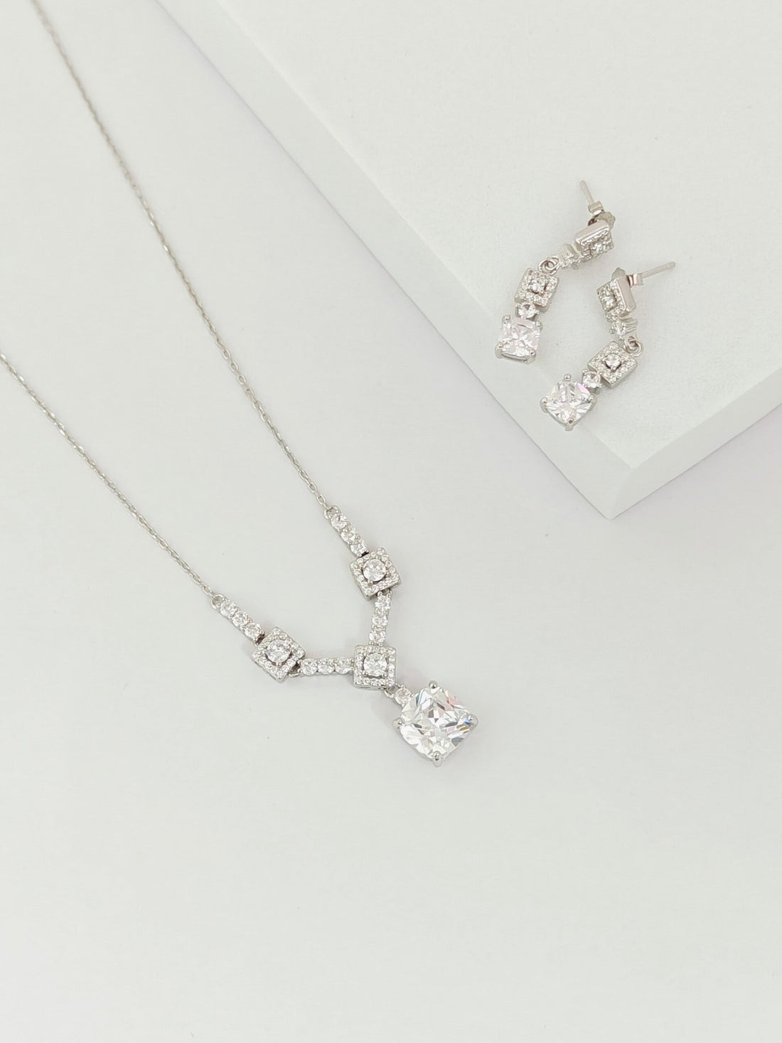 Silver necklace and earrings on a light gray background