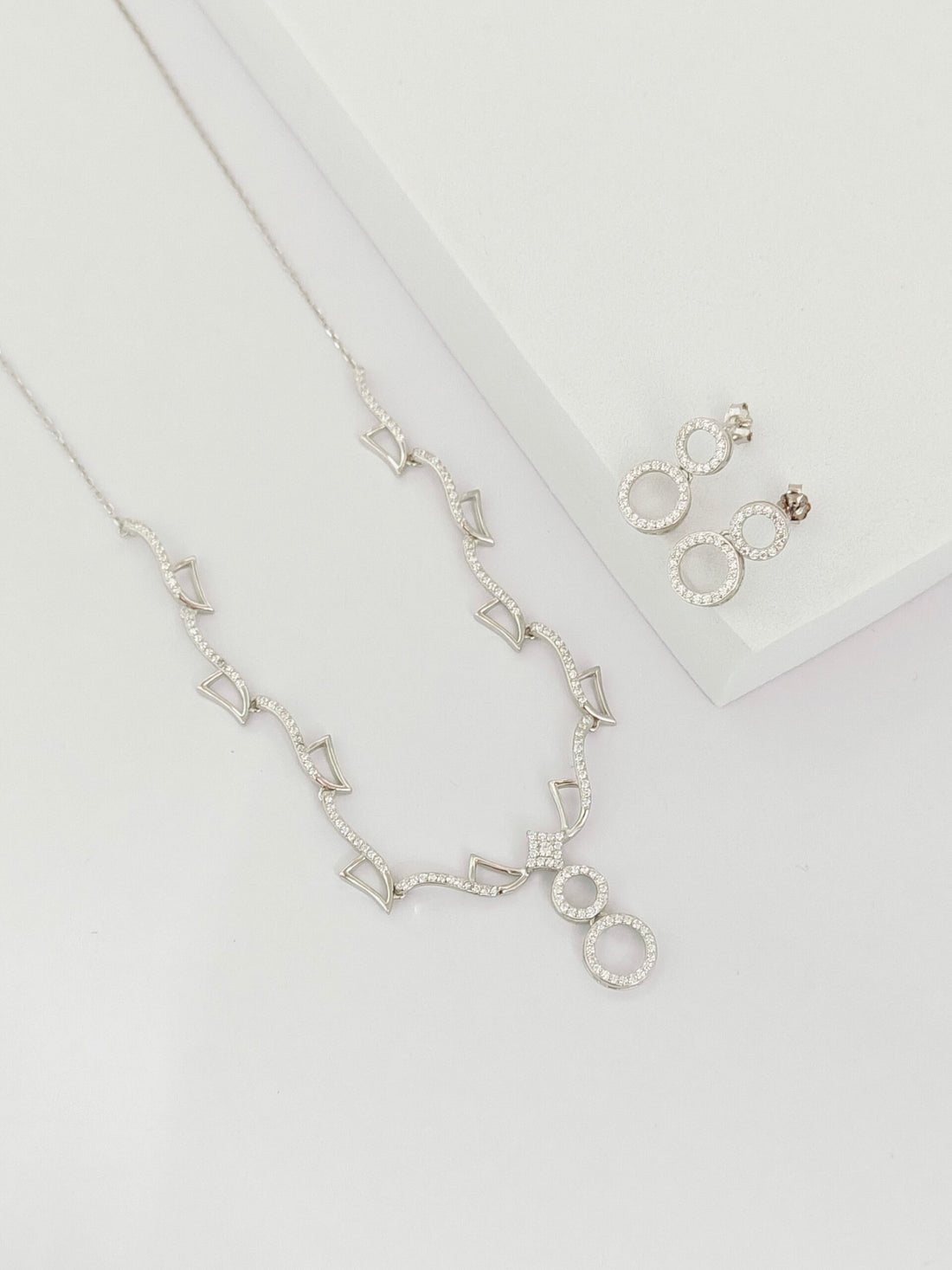 Silver necklace and earrings on a light gray background
