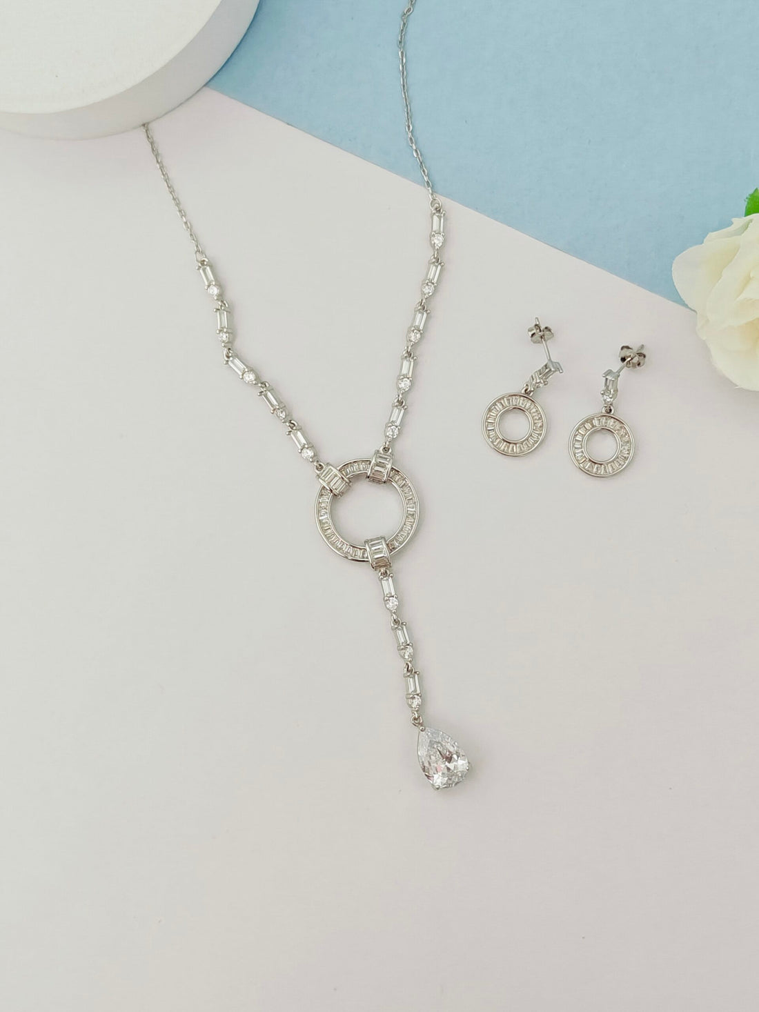 Silver necklace and earrings on a light gray and blue background