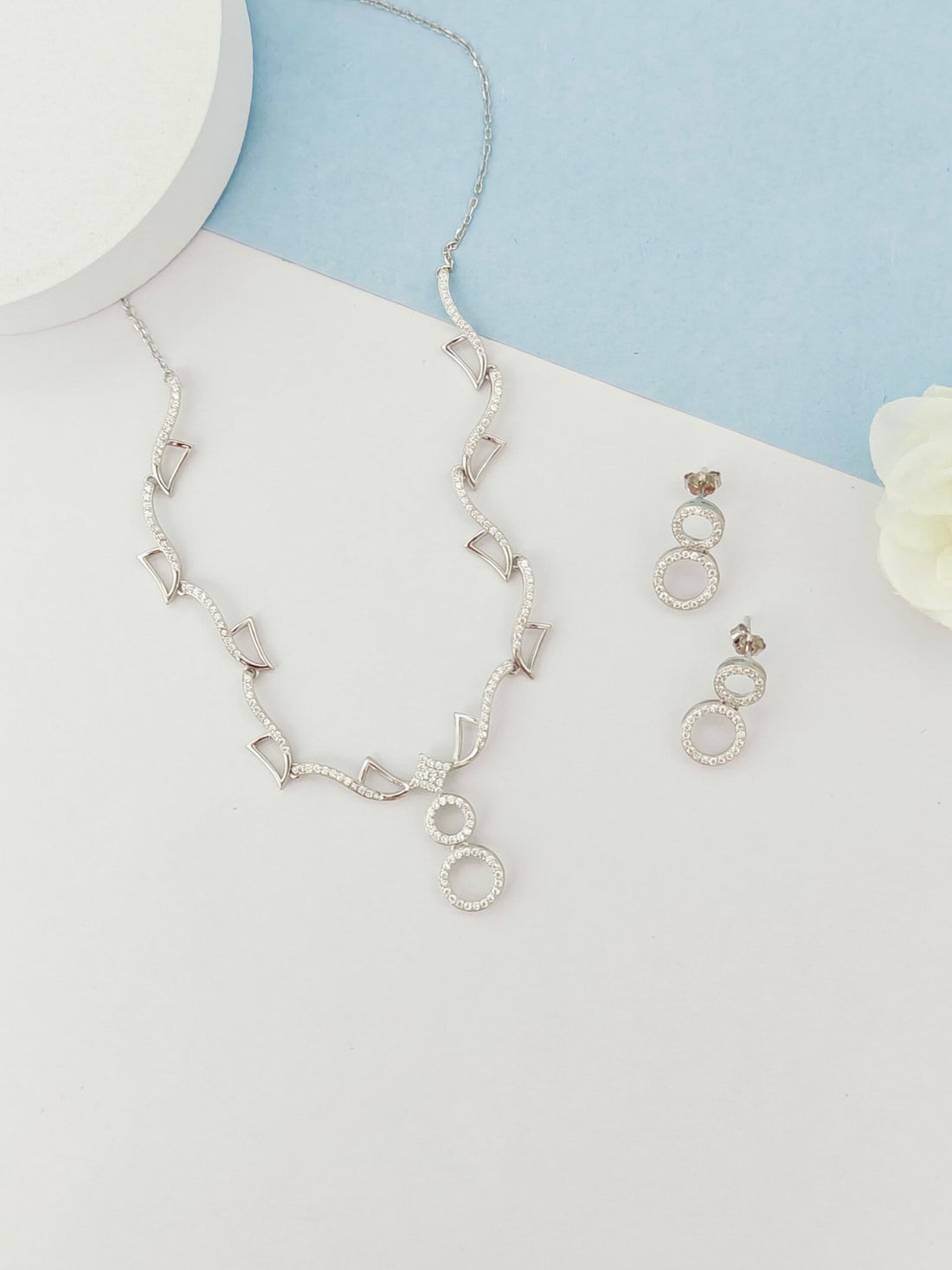 Silver necklace and earrings on a light blue and white background