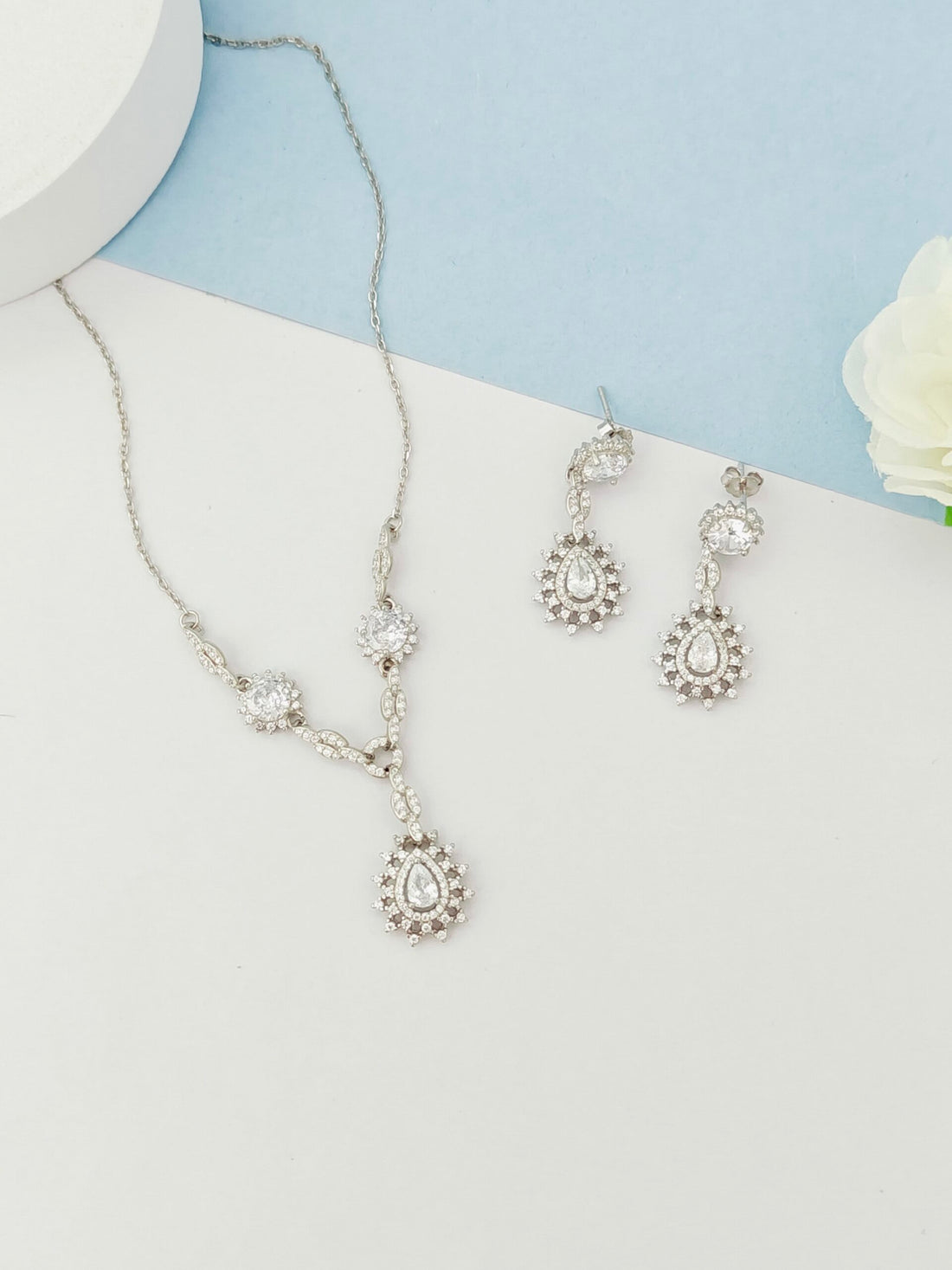 Silver necklace and earrings set on a white surface with a light blue background