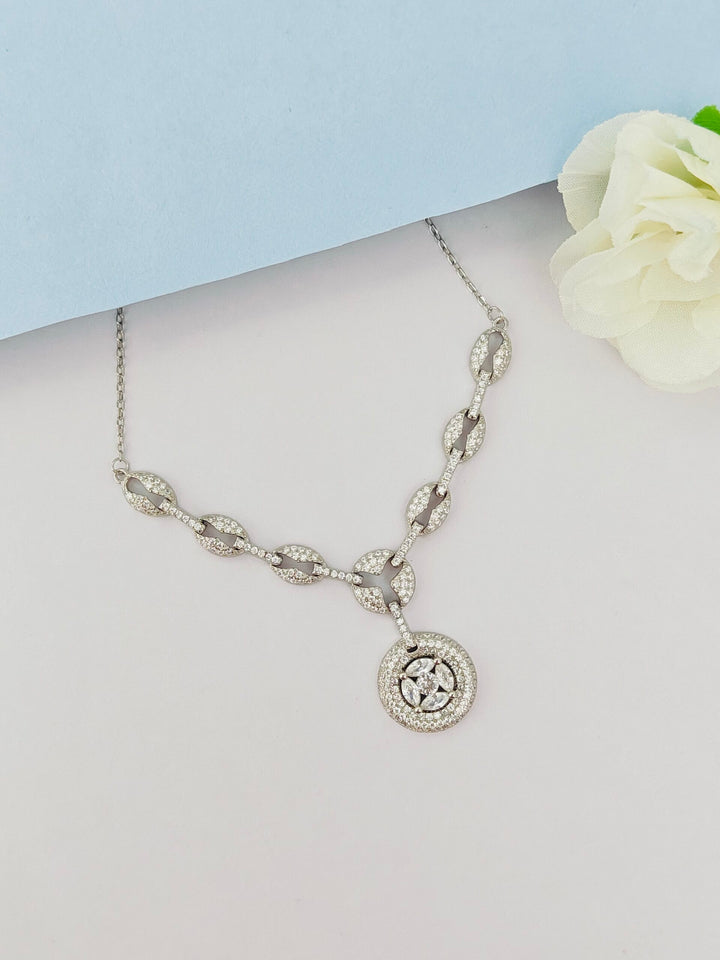 Silver necklace with a circular pendant on a light gray surface with a white flower.