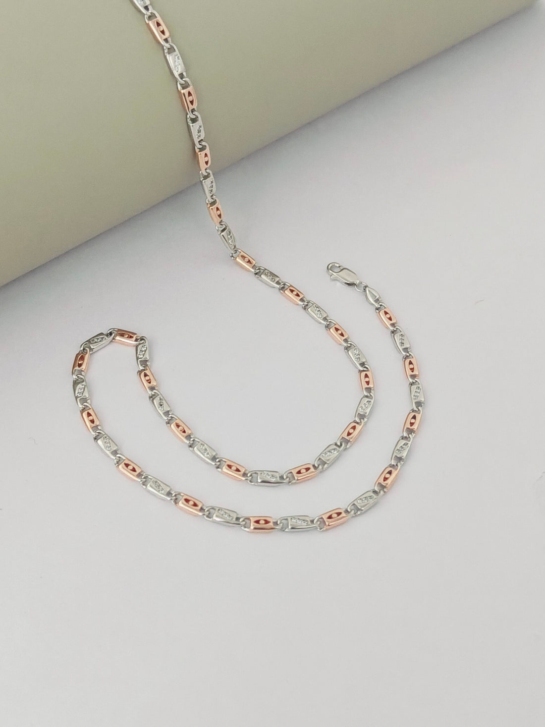 Two rose gold and silver chain necklaces on a light gray surface.