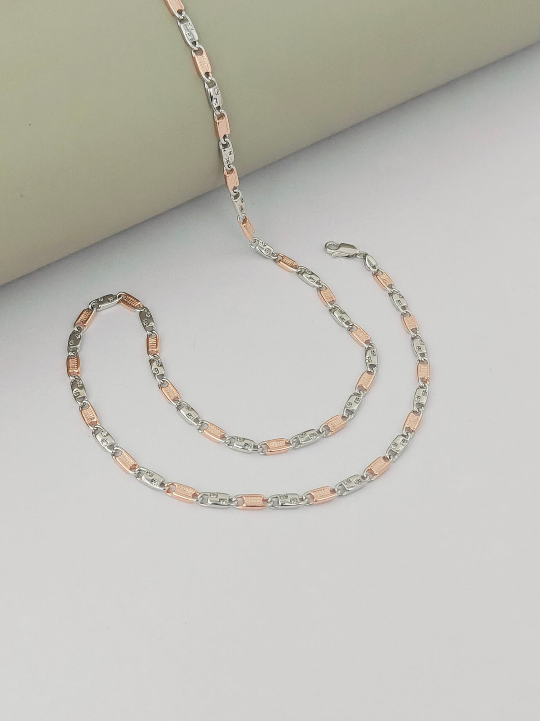 Two necklaces on a light gray surface, one silver and one rose gold.