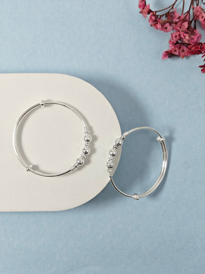 Silver hoop earrings with bead detailing on a light blue background with pink flowers.