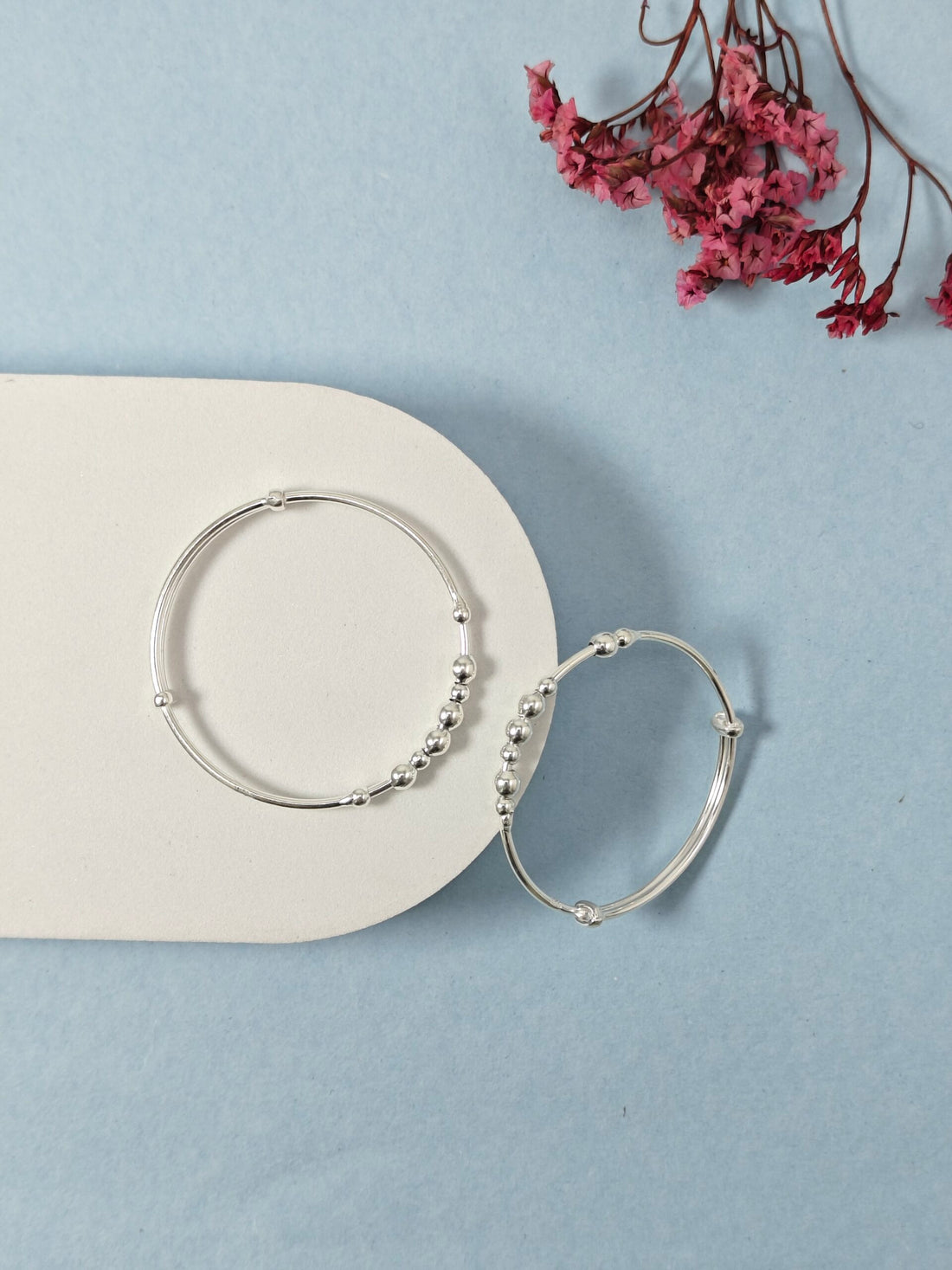 Silver hoop earrings on a light blue surface with pink flowers in the background