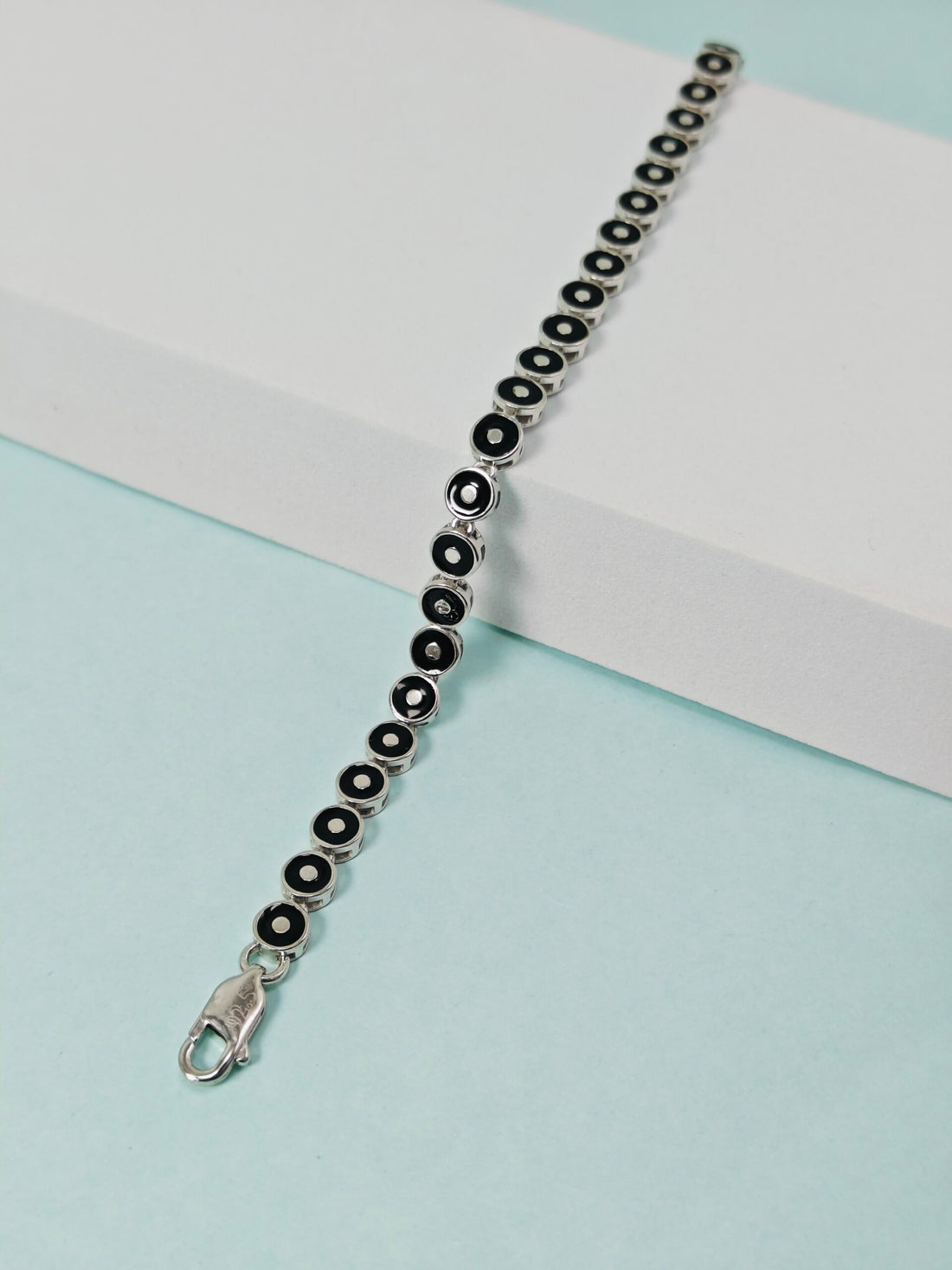 Silver bracelet with black beads on a light blue background