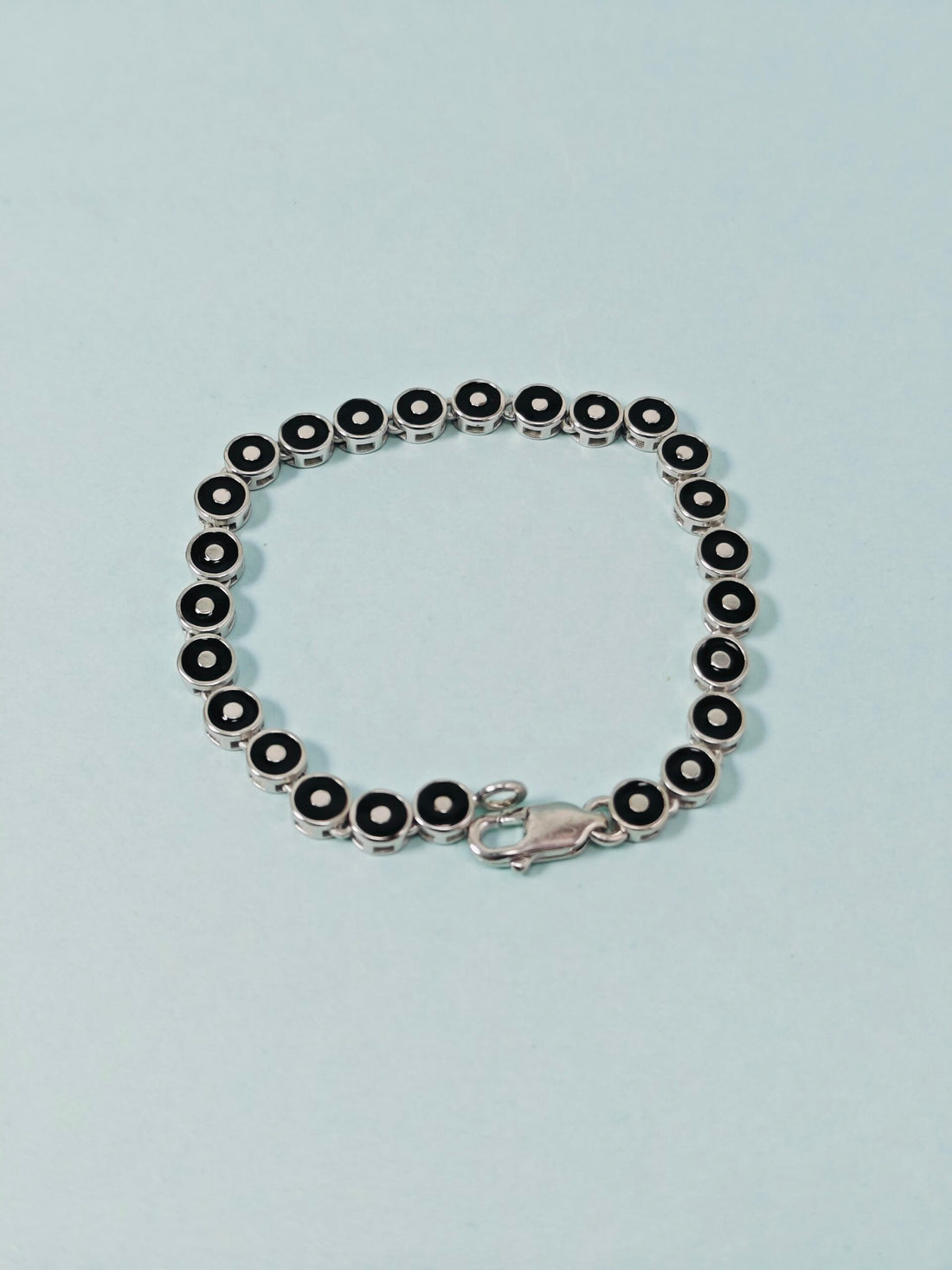 Silver bracelet with black beads on a light blue background