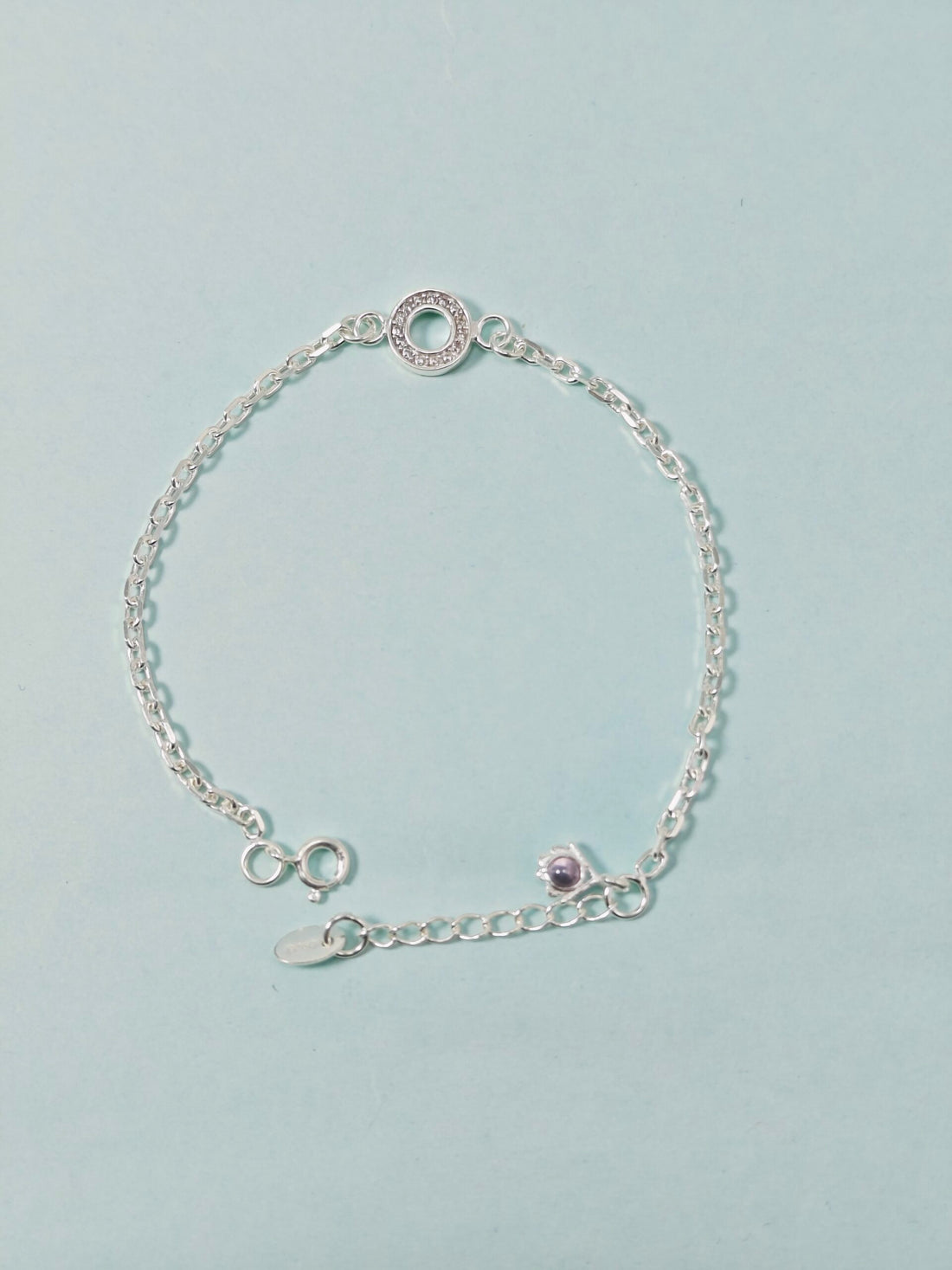 Silver bracelet with a purple gemstone on a light blue background