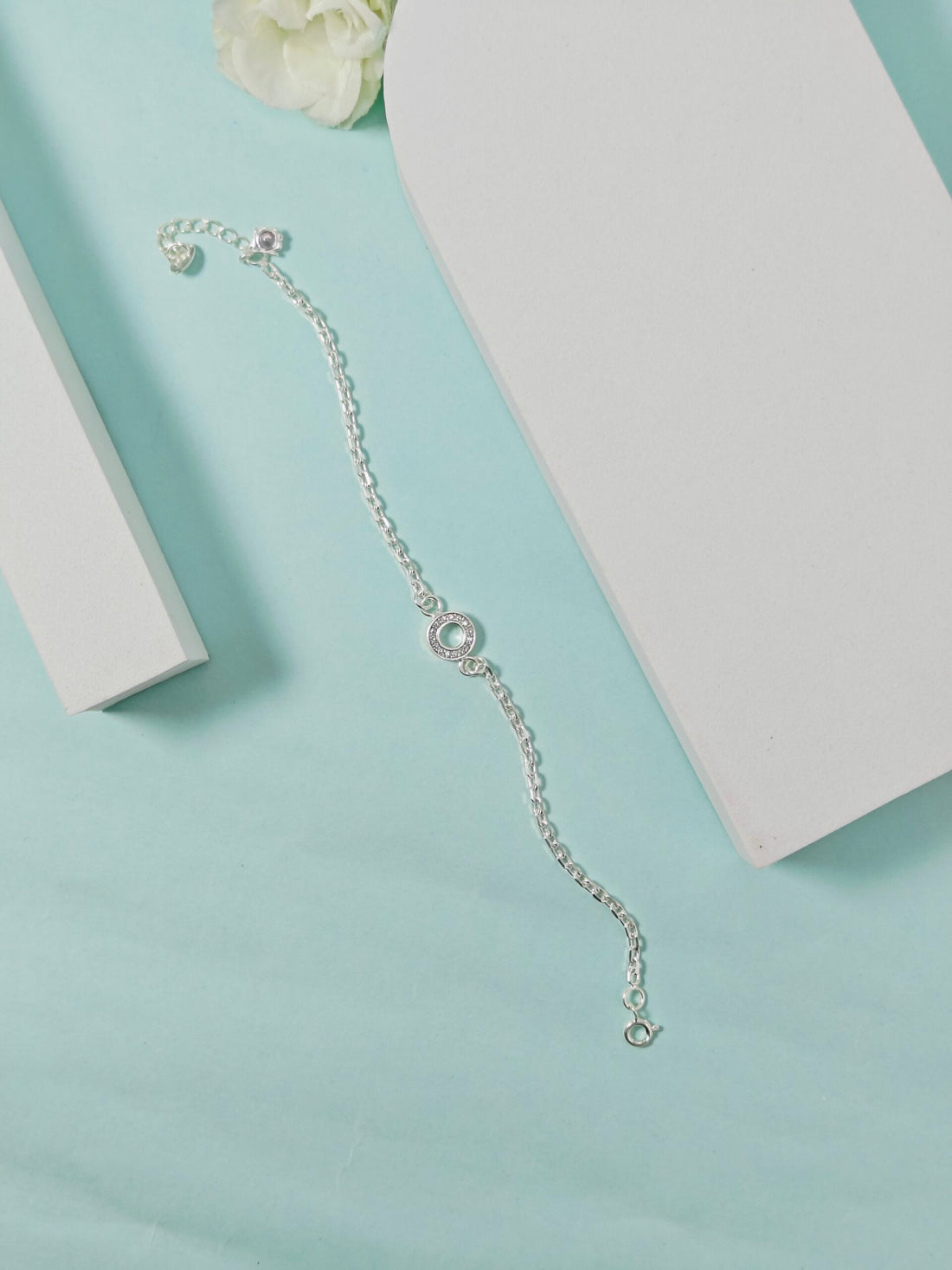 Silver bracelet on a light blue surface with a white flower and box in the background