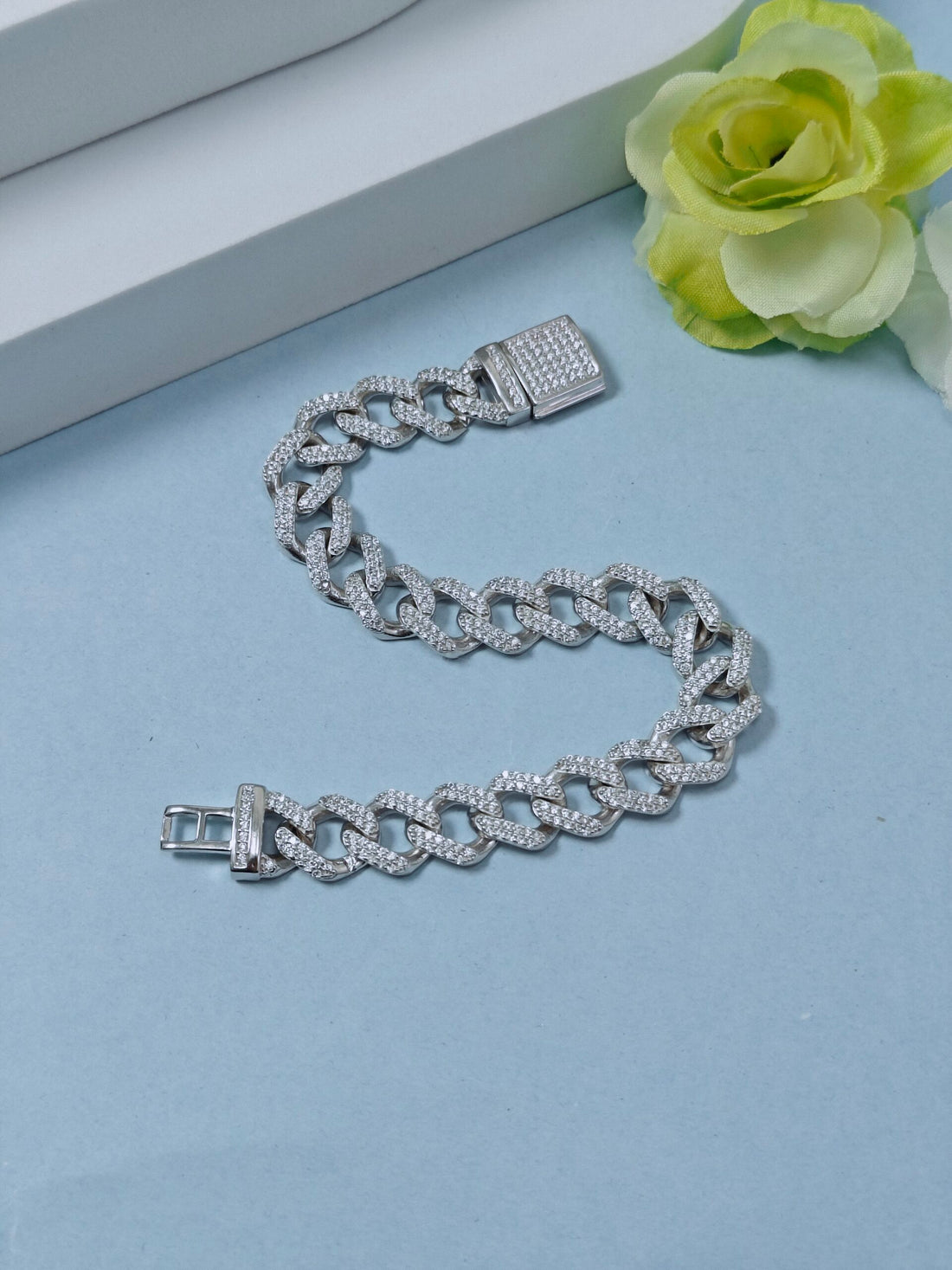 Silver chain bracelet on a light blue surface with a green flower.