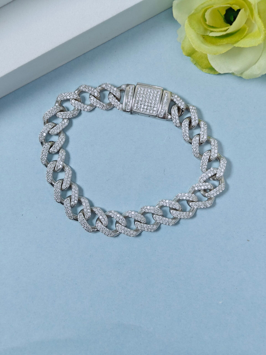 Silver chain bracelet on a light blue surface with a yellow flower.