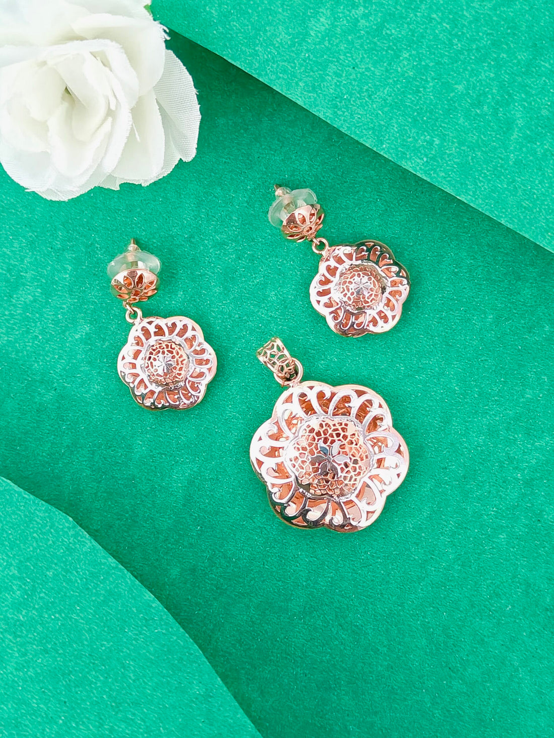 Rose gold floral earrings on a green background with a white flower.