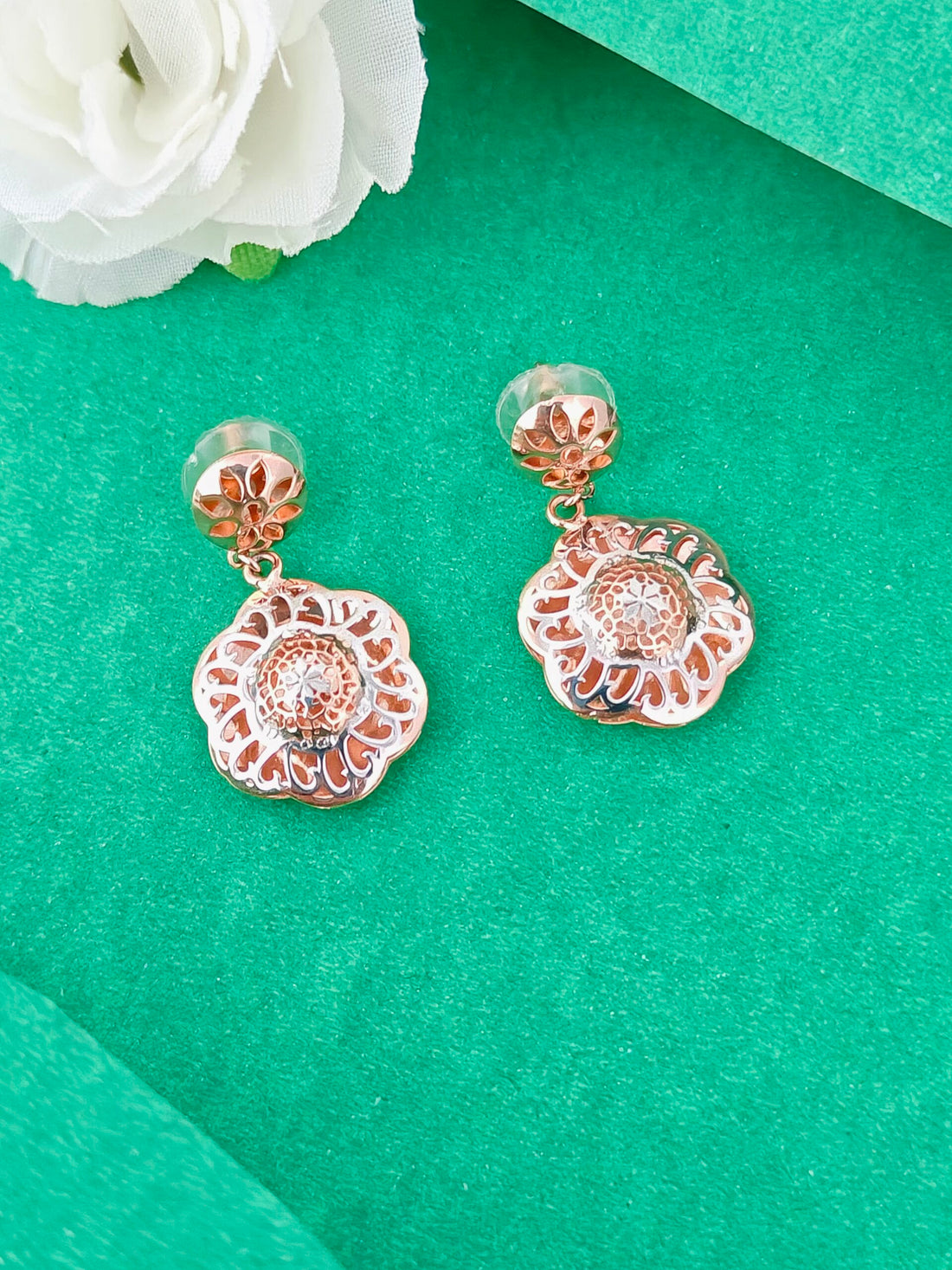 Rose gold floral earrings on a green background with a white flower.