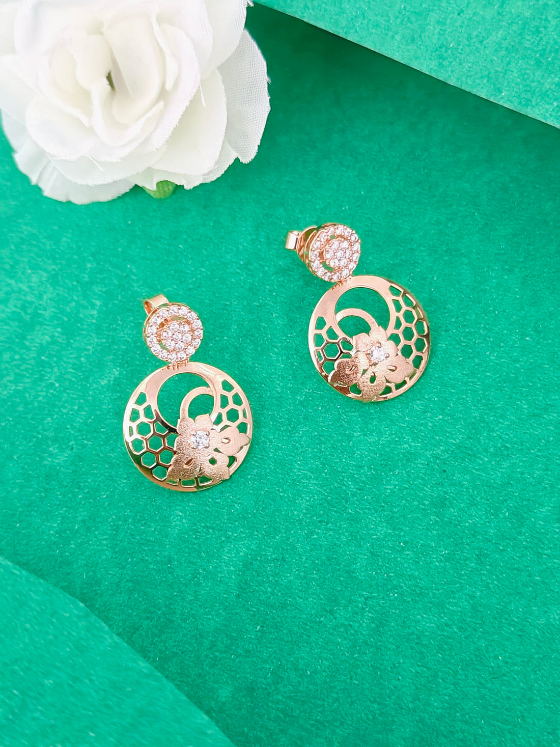 Gold earrings with floral design on a green surface with a white flower.
