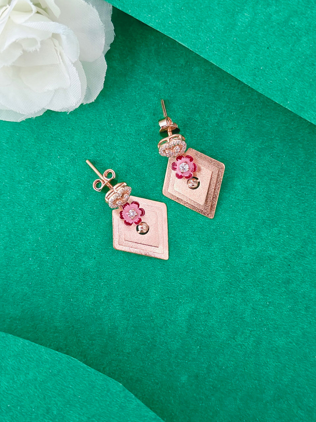 Rose gold earrings with floral designs on a green surface with a white flower.