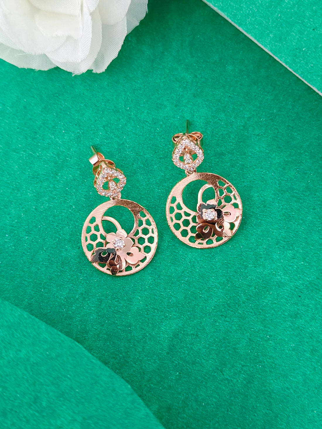 Rose gold earrings with floral designs on a green background