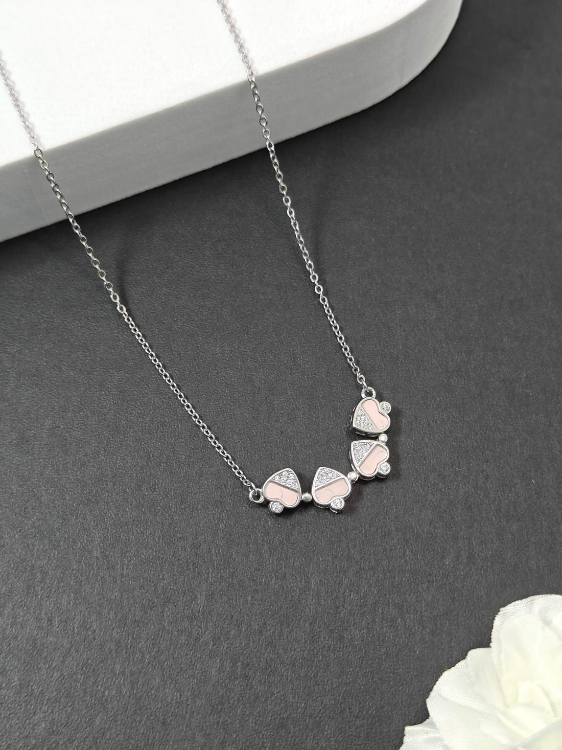 Silver necklace with leaf-shaped pendants on a gray surface with a white flower.