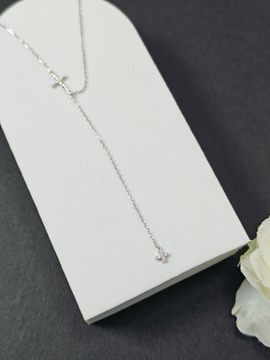Silver necklace with a small pendant on a white card against a dark background