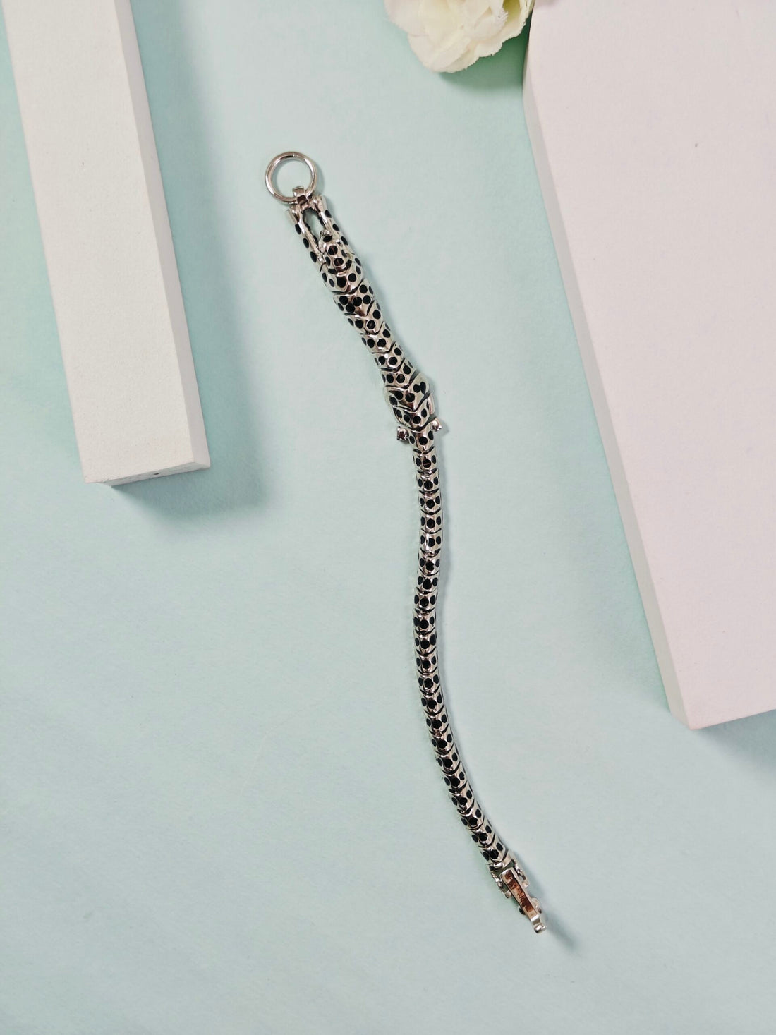 Silver chain bracelet on a light blue surface with a white flower and pink box in the background