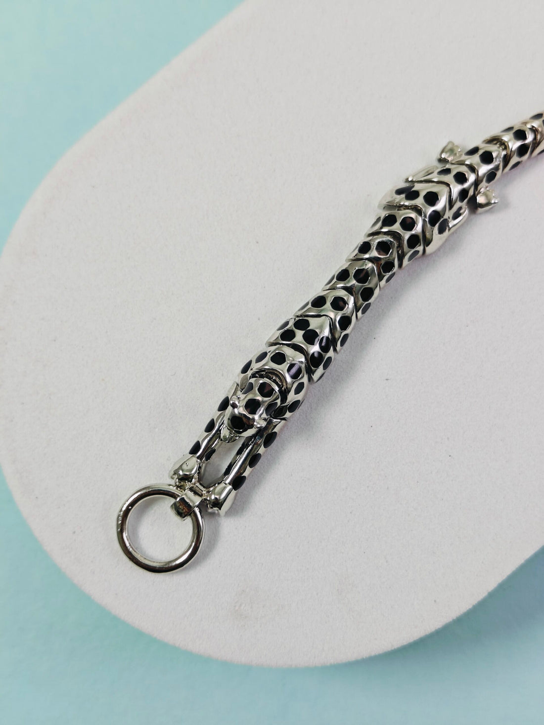 Silver chain with a unique design on a white platform against a light blue background