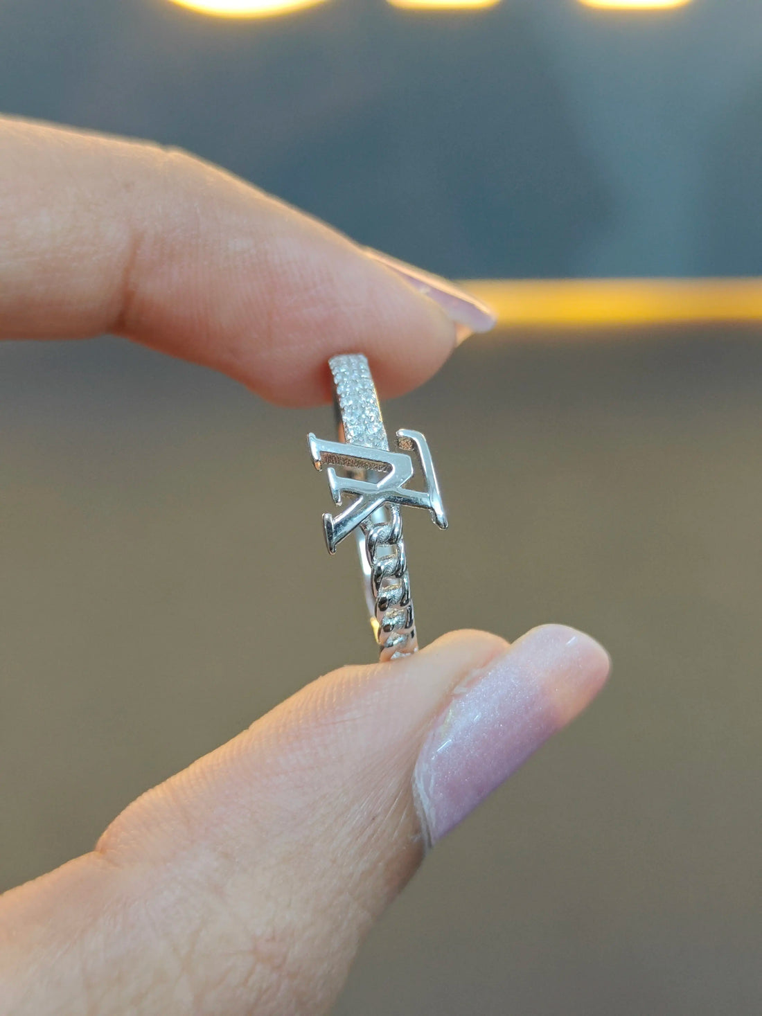 Silver ring with a unique design held between fingers against a blurred background
