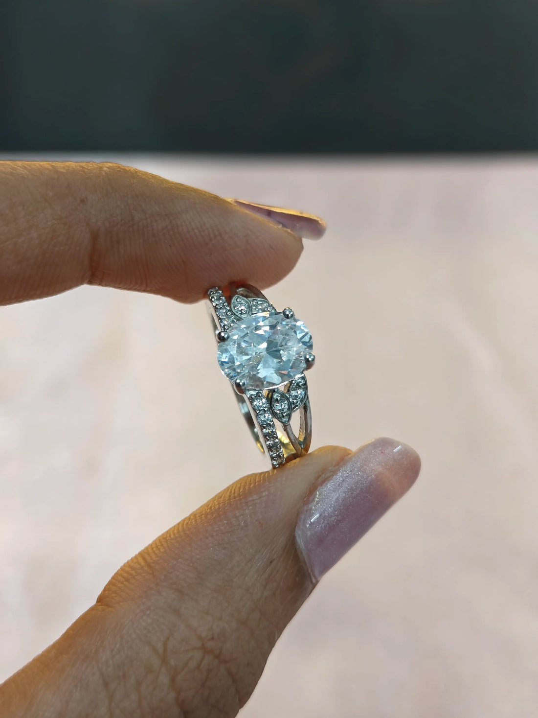 Diamond ring held between fingers against a neutral background