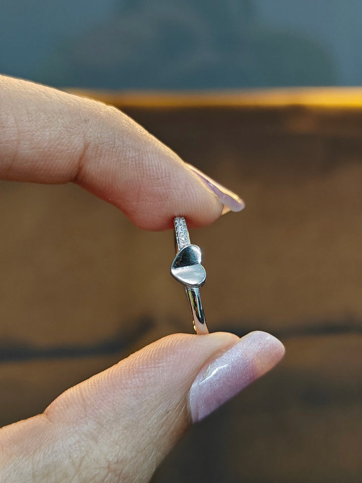 Silver ring with a unique design held between two fingers against a blurred background