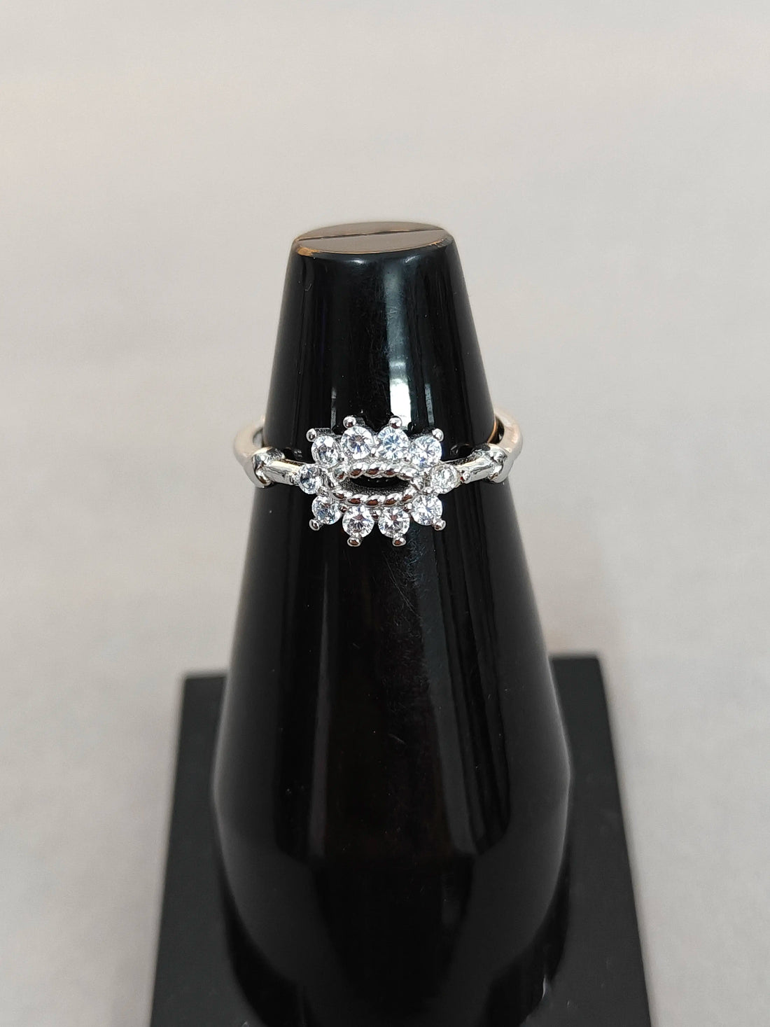 Silver ring with diamonds on a black stand against a light gray background