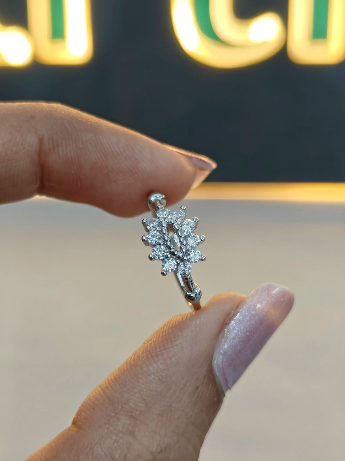 Silver earring held between fingers with a blurred background