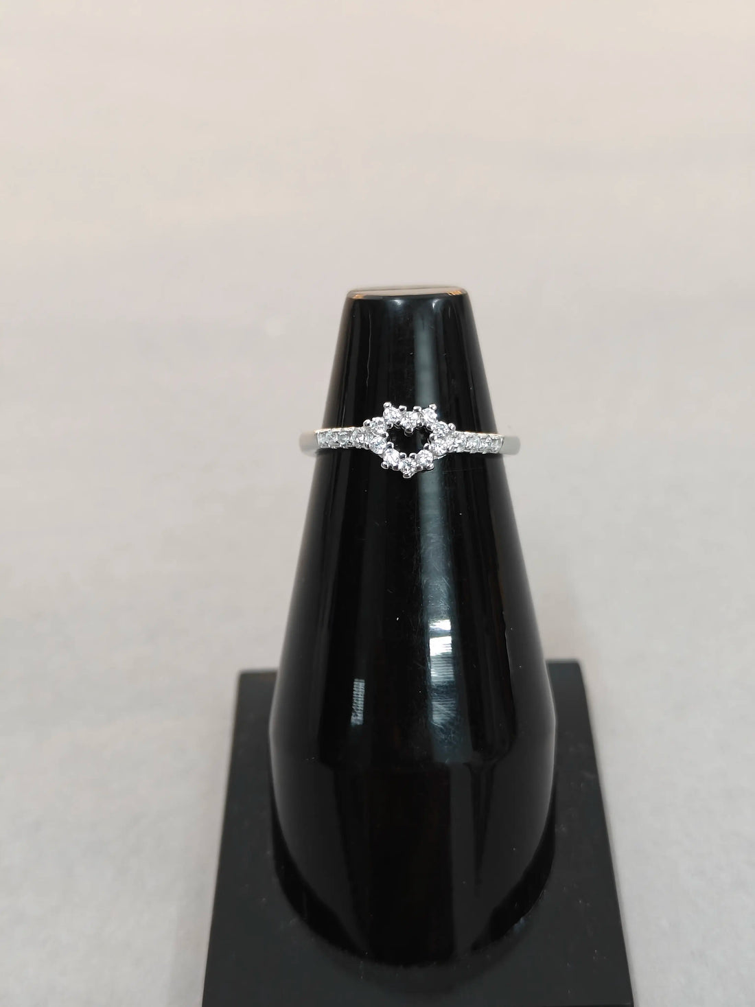 Silver ring with a heart-shaped center on a black stand against a light gray background