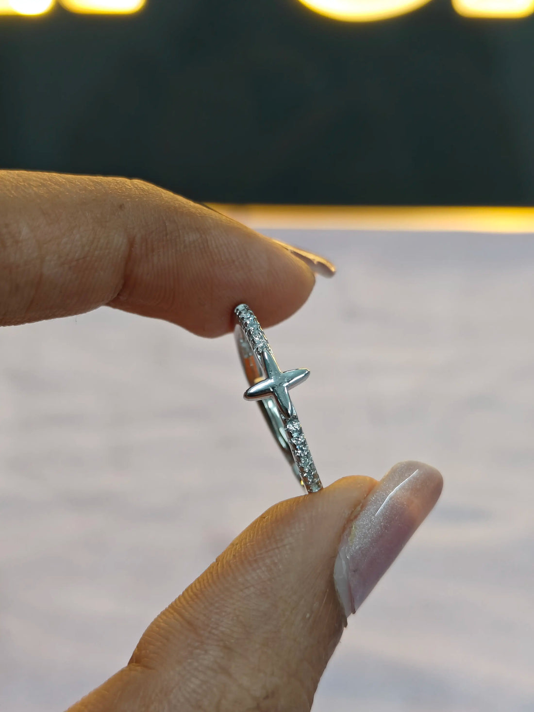 Silver cross necklace held by a hand against a blurred background