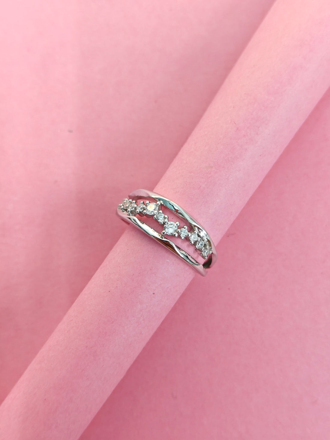 Silver ring with small diamonds on a pink fabric background