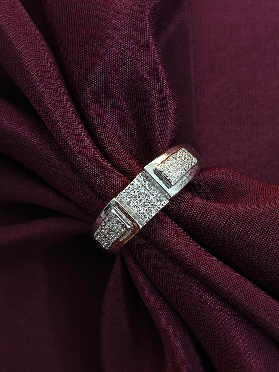 Silver ring with diamonds on a burgundy fabric background