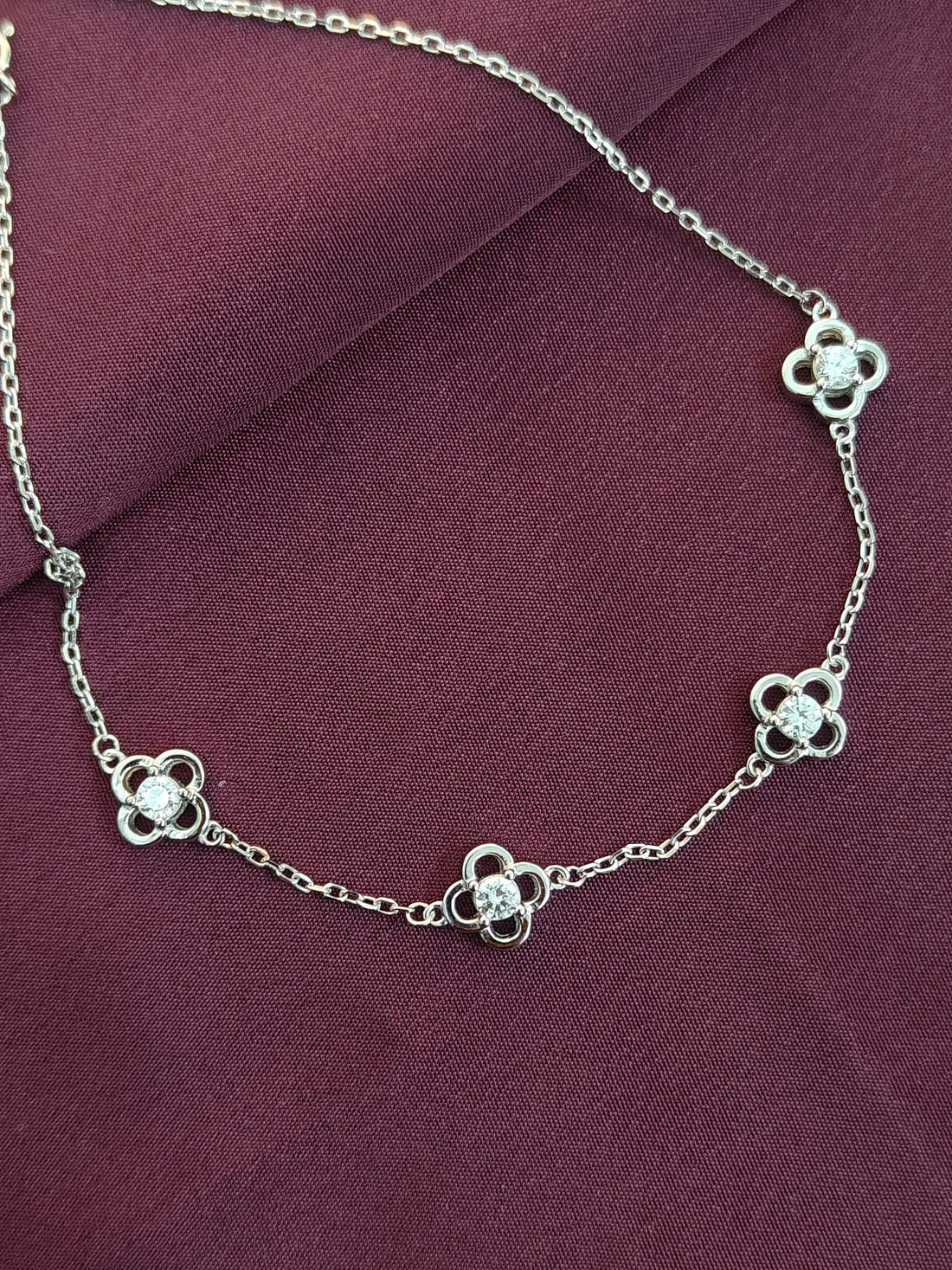 Silver necklace with floral designs on a purple fabric background