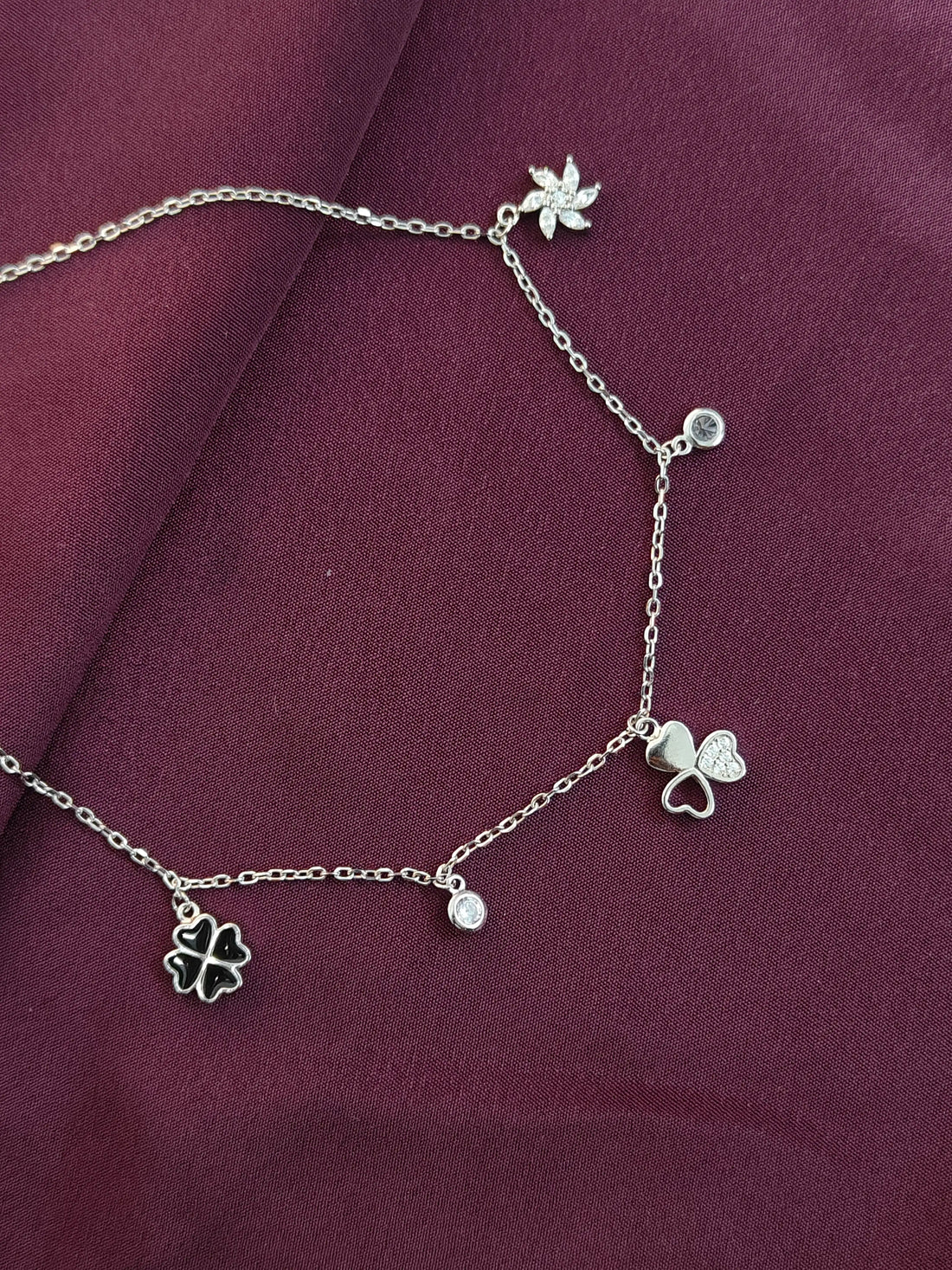 Silver anklet with charms on a purple fabric background