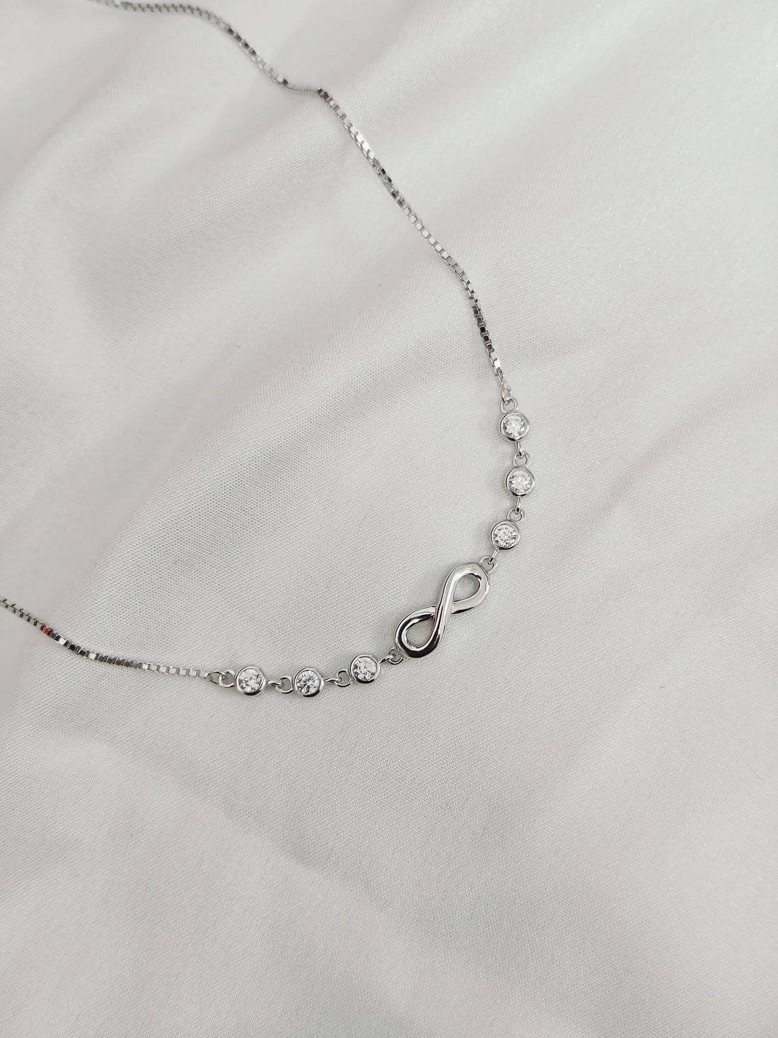 Silver necklace with a heart and infinity symbol on a light gray background