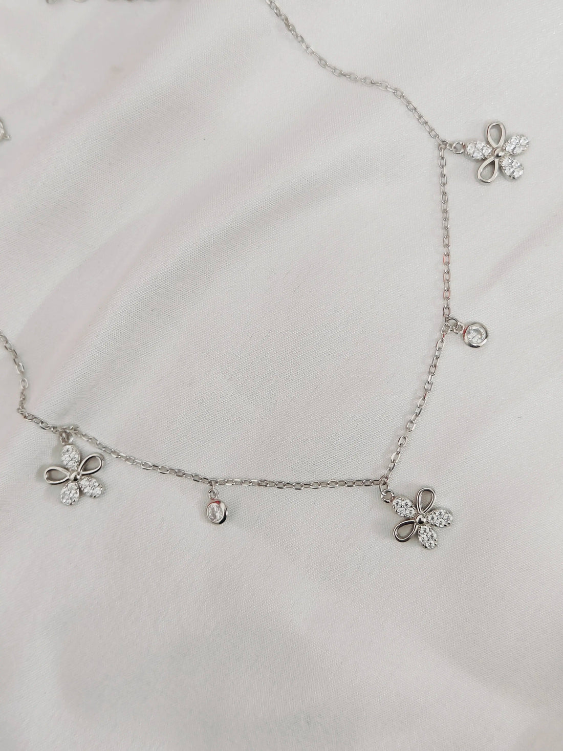 Silver necklace with floral pendants on a light gray background