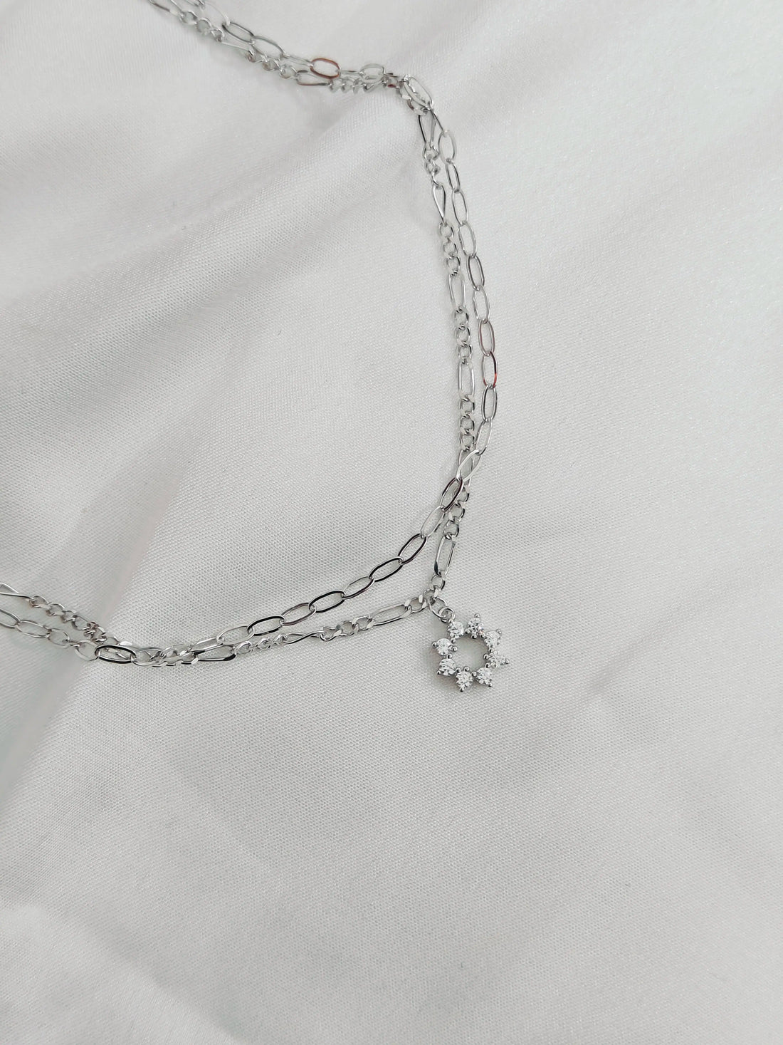 Silver chain necklace with a small round pendant on a light gray background