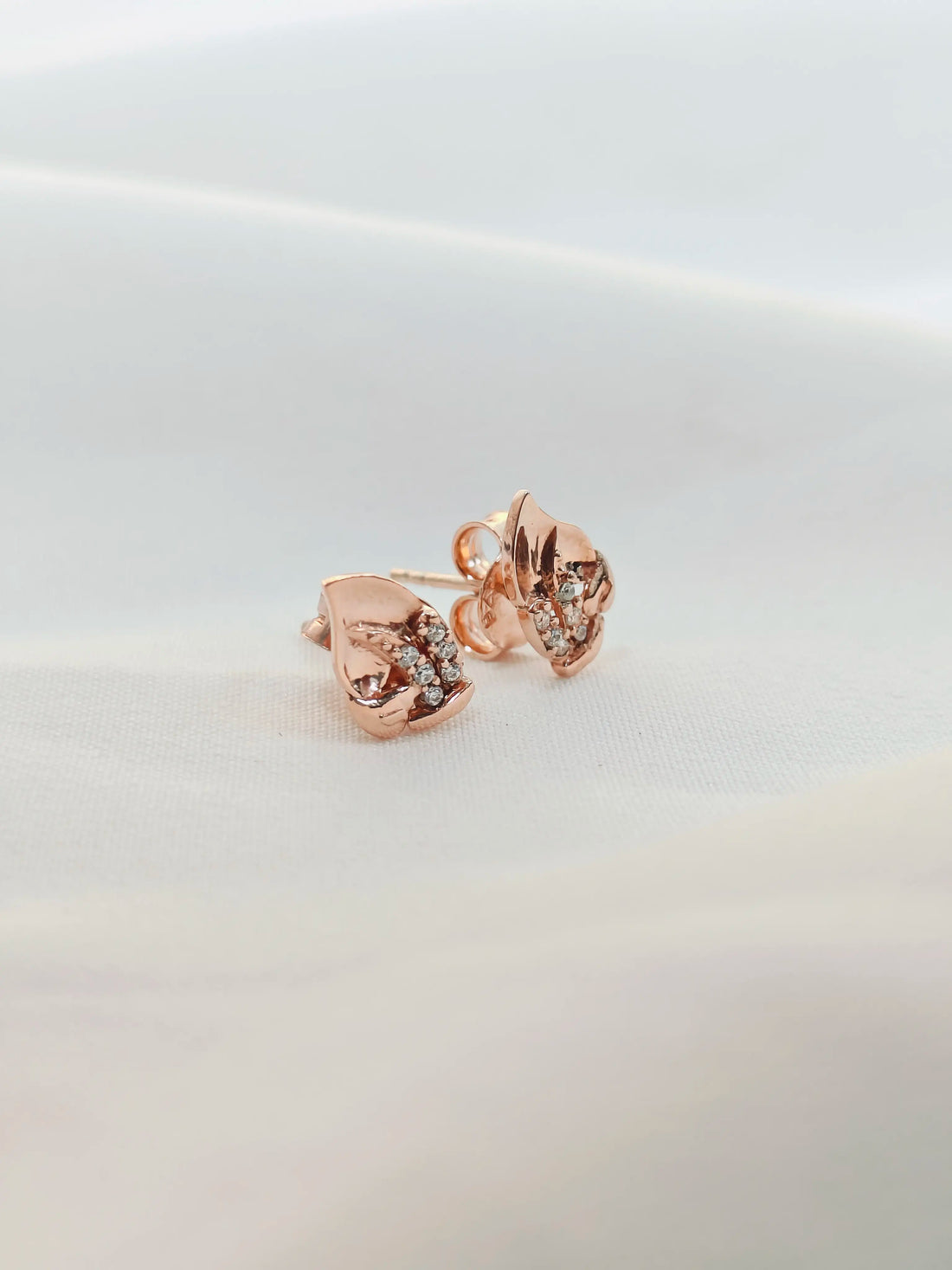 Rose gold earrings with clear gemstones on a light gray background
