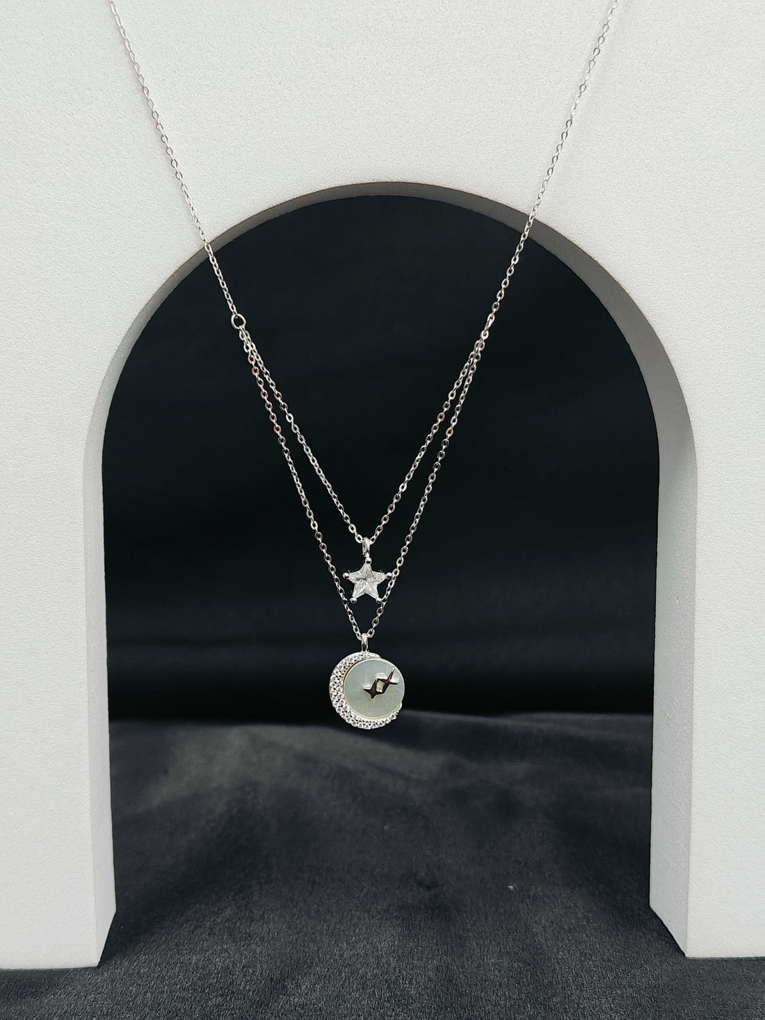 Two silver necklaces with star and circular pendants on a black background