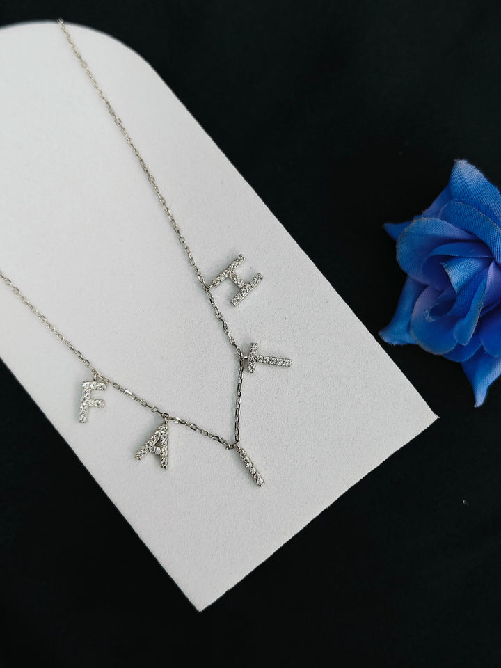 Silver necklace with letter pendants on a white card with a blue flower