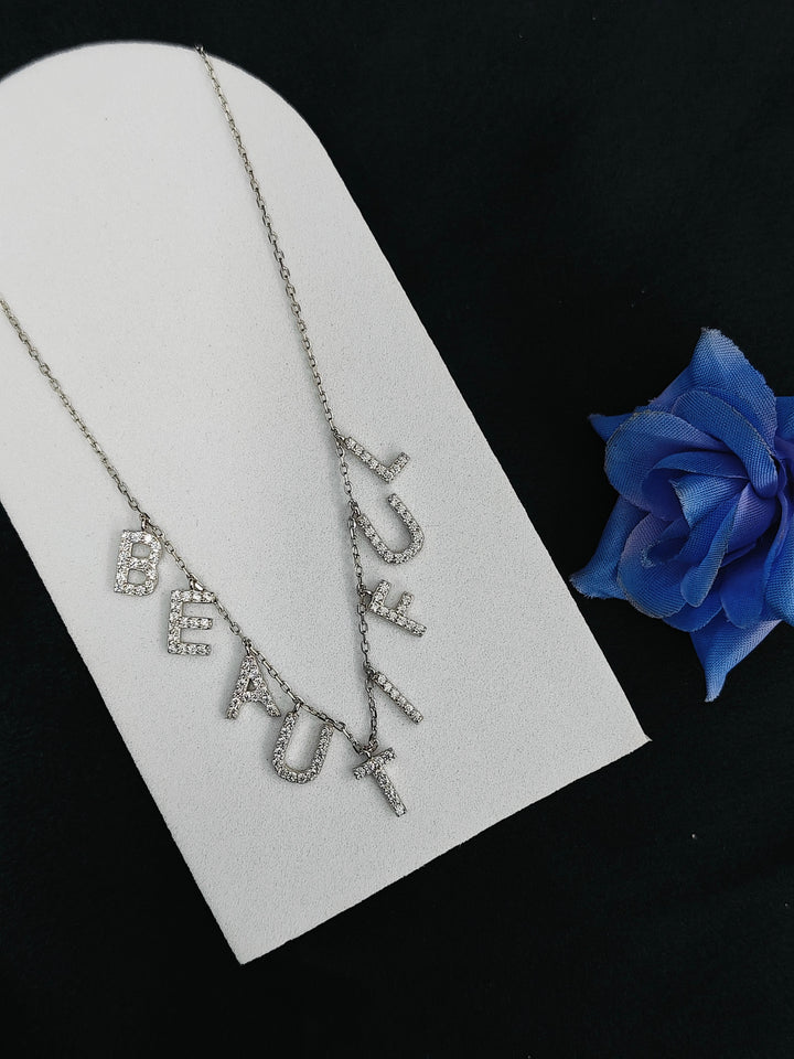 Silver necklace with 'BEFAUX' pendant on a white card with a blue rose.