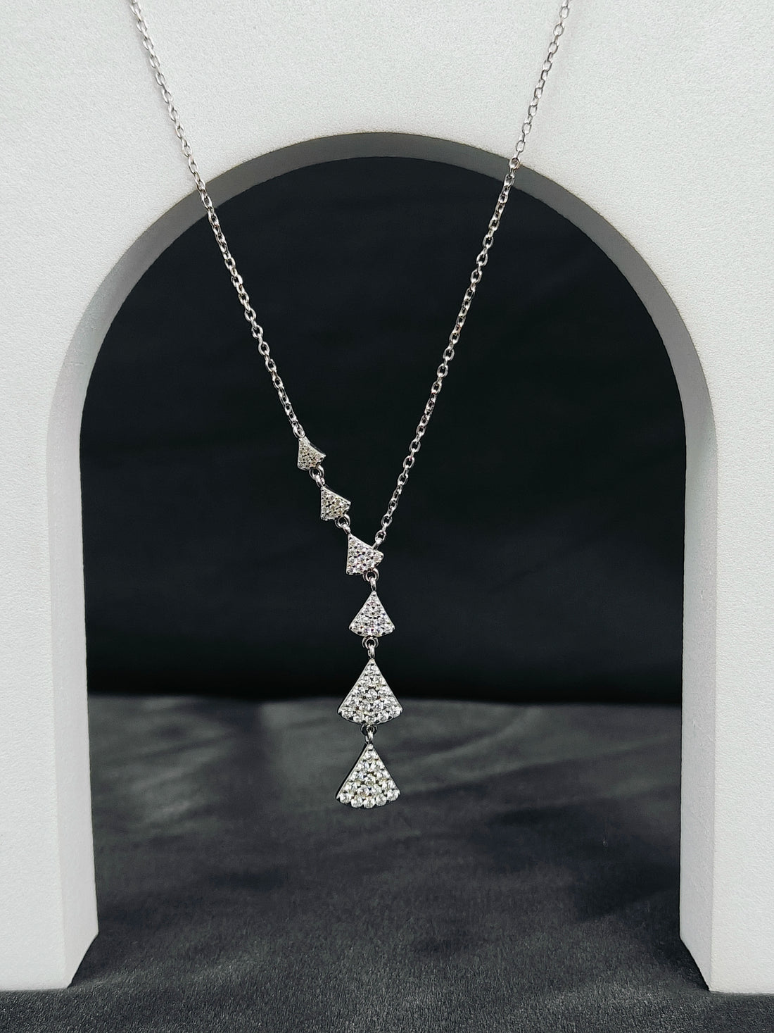Silver necklace with diamond pendants hanging in front of a white archway.