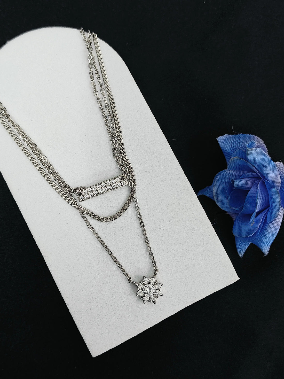 Silver necklace on a white stand with a blue rose on a black background