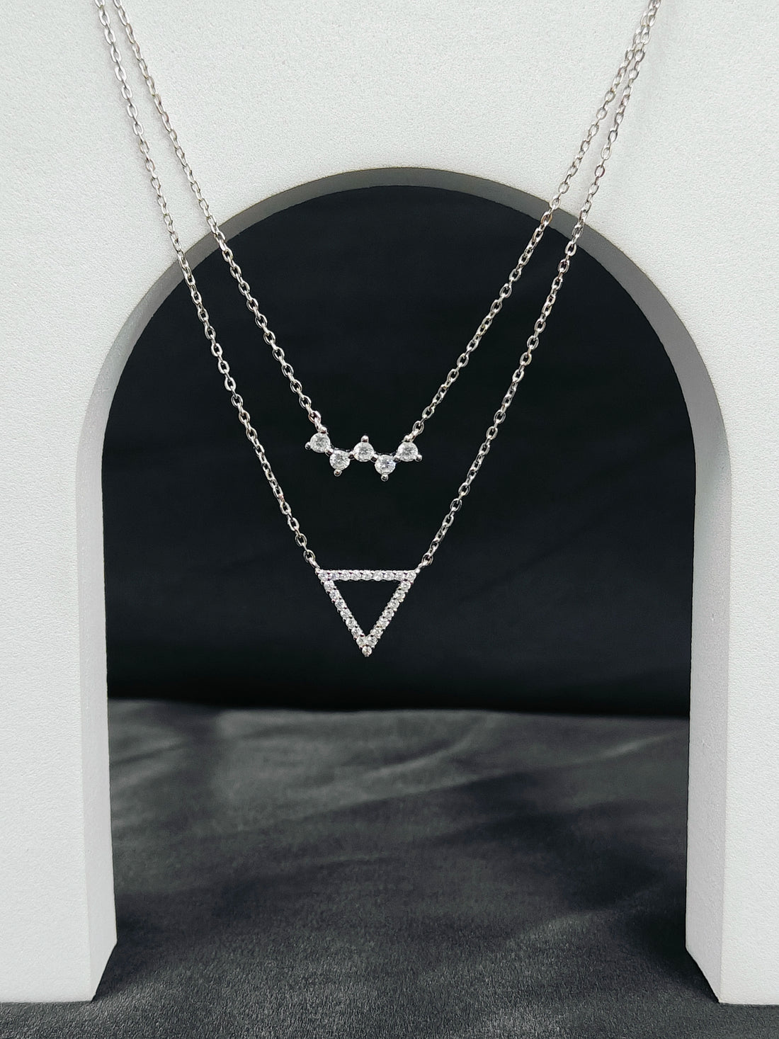 Two silver necklaces with geometric pendants on a dark background