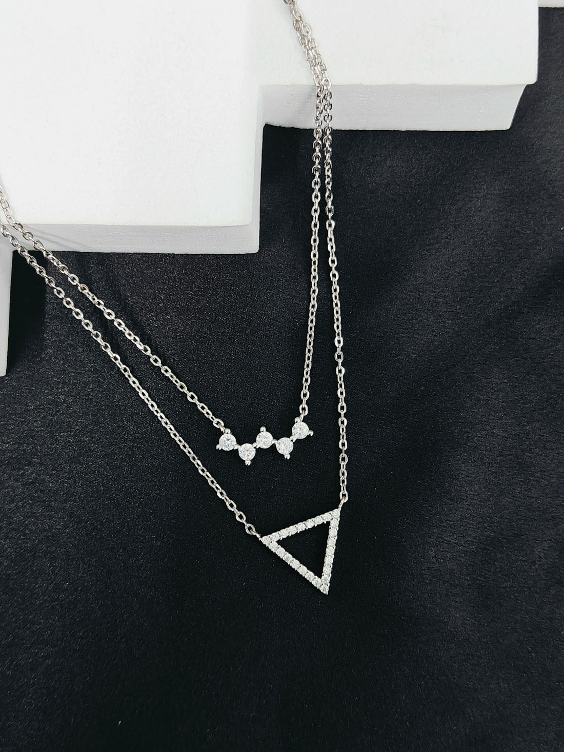 Two silver necklaces with geometric pendants on a black surface.