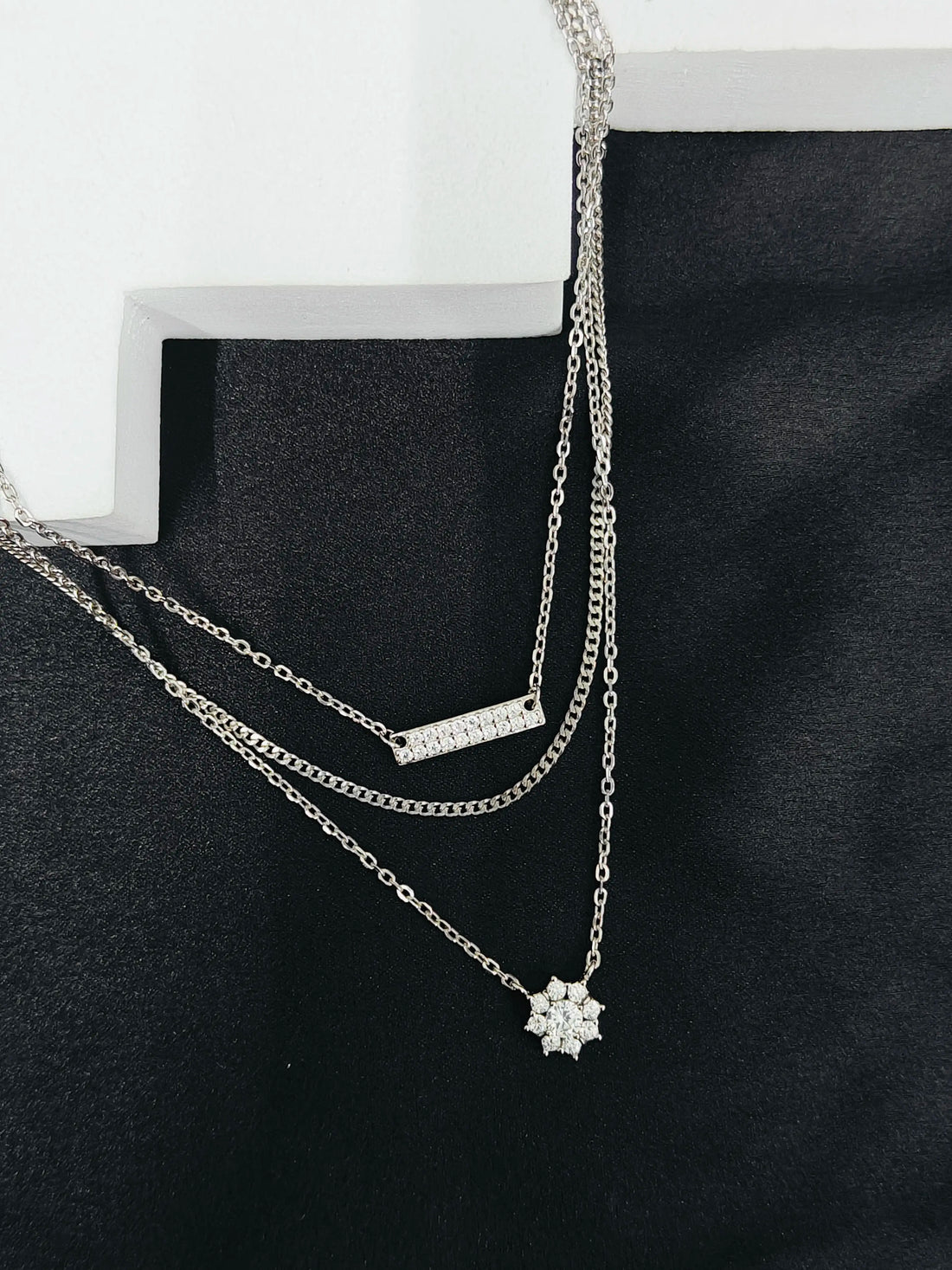 Two silver necklaces on a black stand with a white background