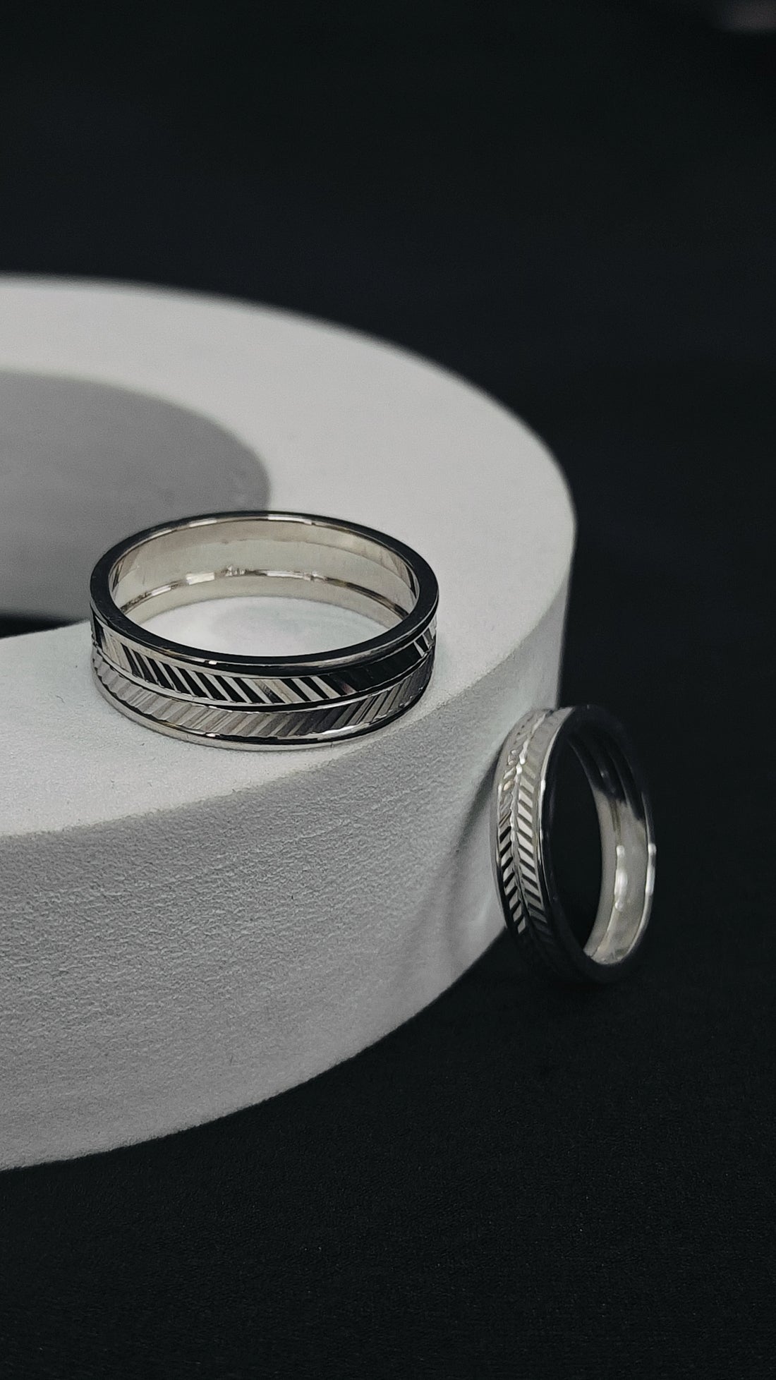 Silver rings with geometric designs on a white cylindrical object against a black background